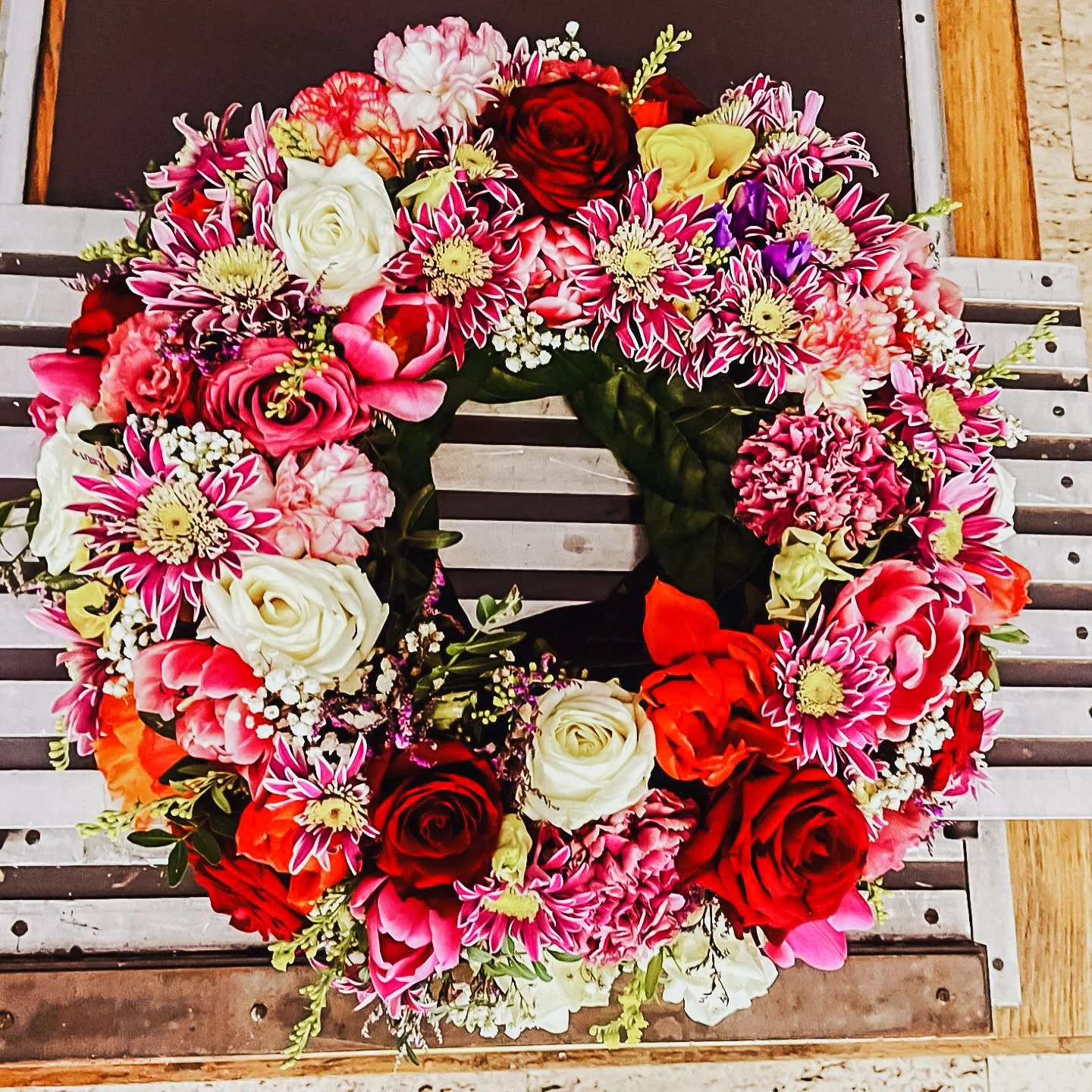 Blumenkranz mit roten, weißen, rosa, und violetten Blumen, auf einem Holzbank