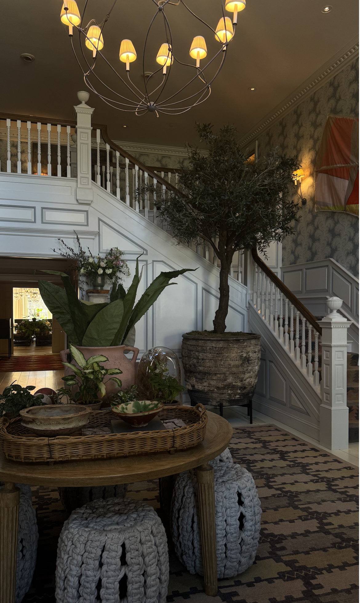 Mayflower Inn interior with a grand white staircase, indoor tree, plants, and elegant decor.