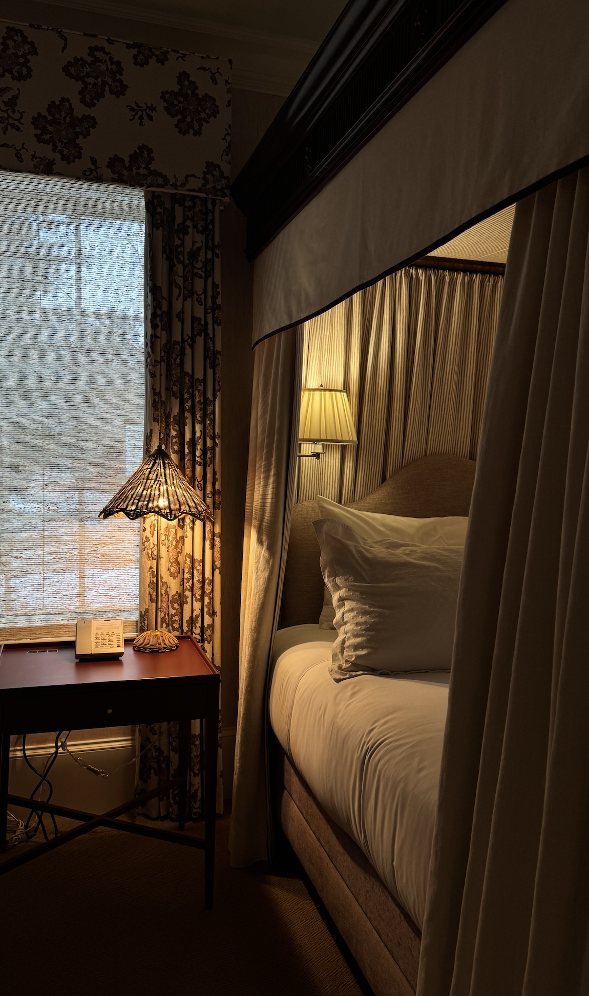 Cozy guest room at the Mayflower Inn with a canopy bed, patterned curtains, and warm bedside lighting.