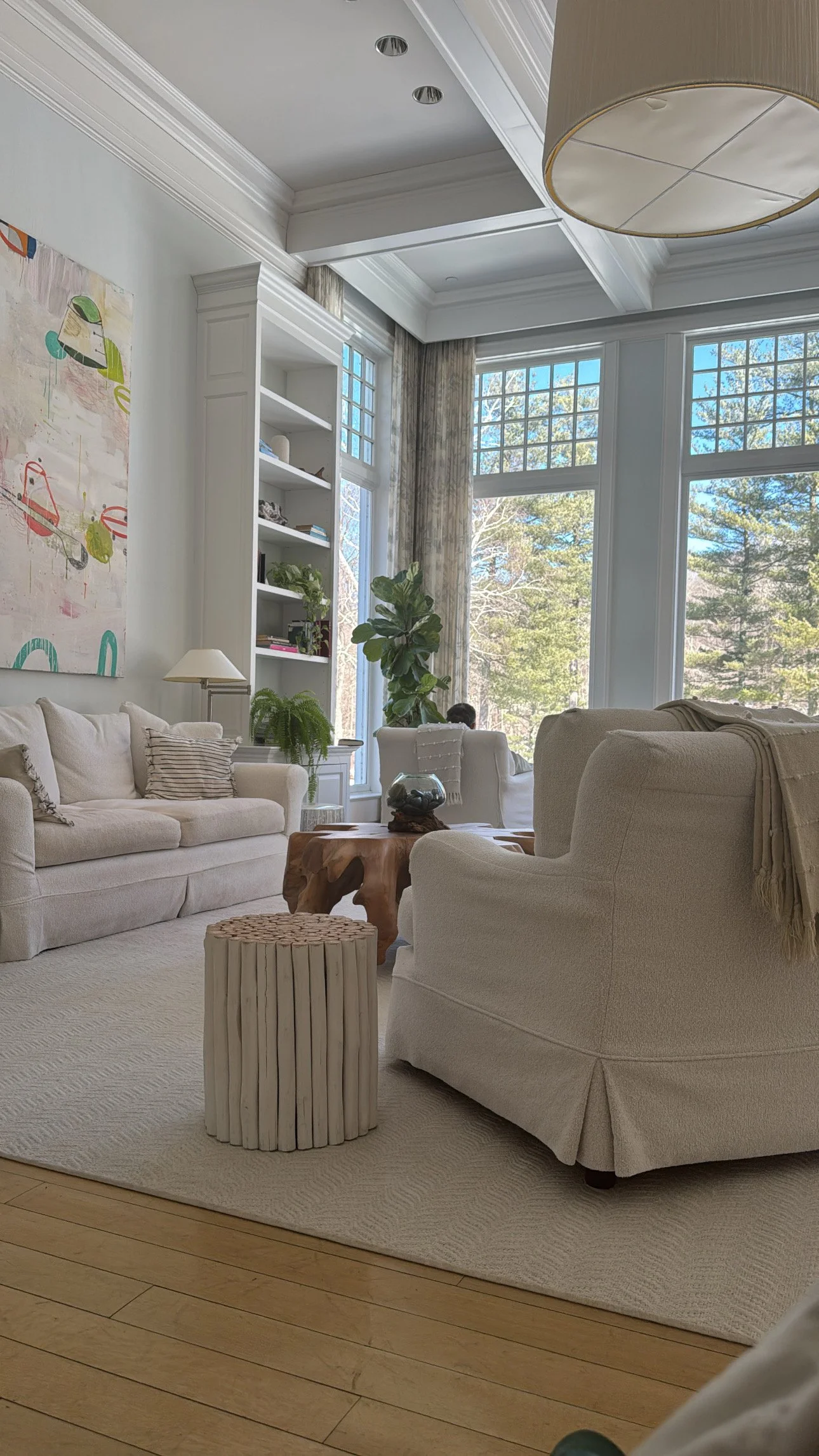 Bright lounge at the Mayflower Inn with large windows, neutral seating, indoor plants, and views of the surrounding trees.