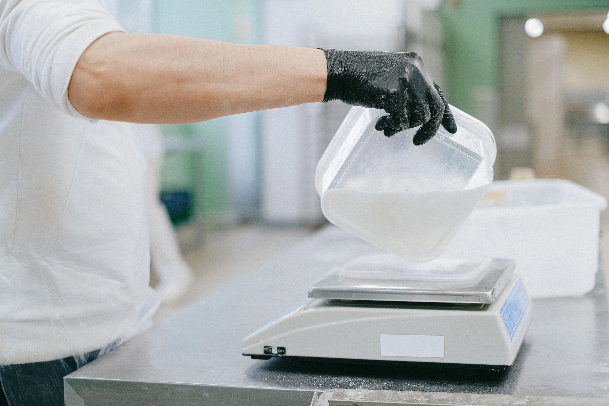 Person wiegt eine Bar-Prep in einem Behälter auf einer Waage ab – als Beispiel für Portionierung, Standards und Kontrolle beim Wareneinsatz in Bars.