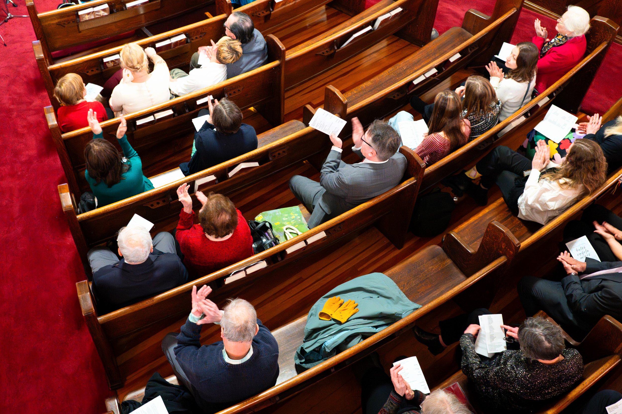 People sitting in wooden pews in a church, engaging in a service or event, some raising their hands.
