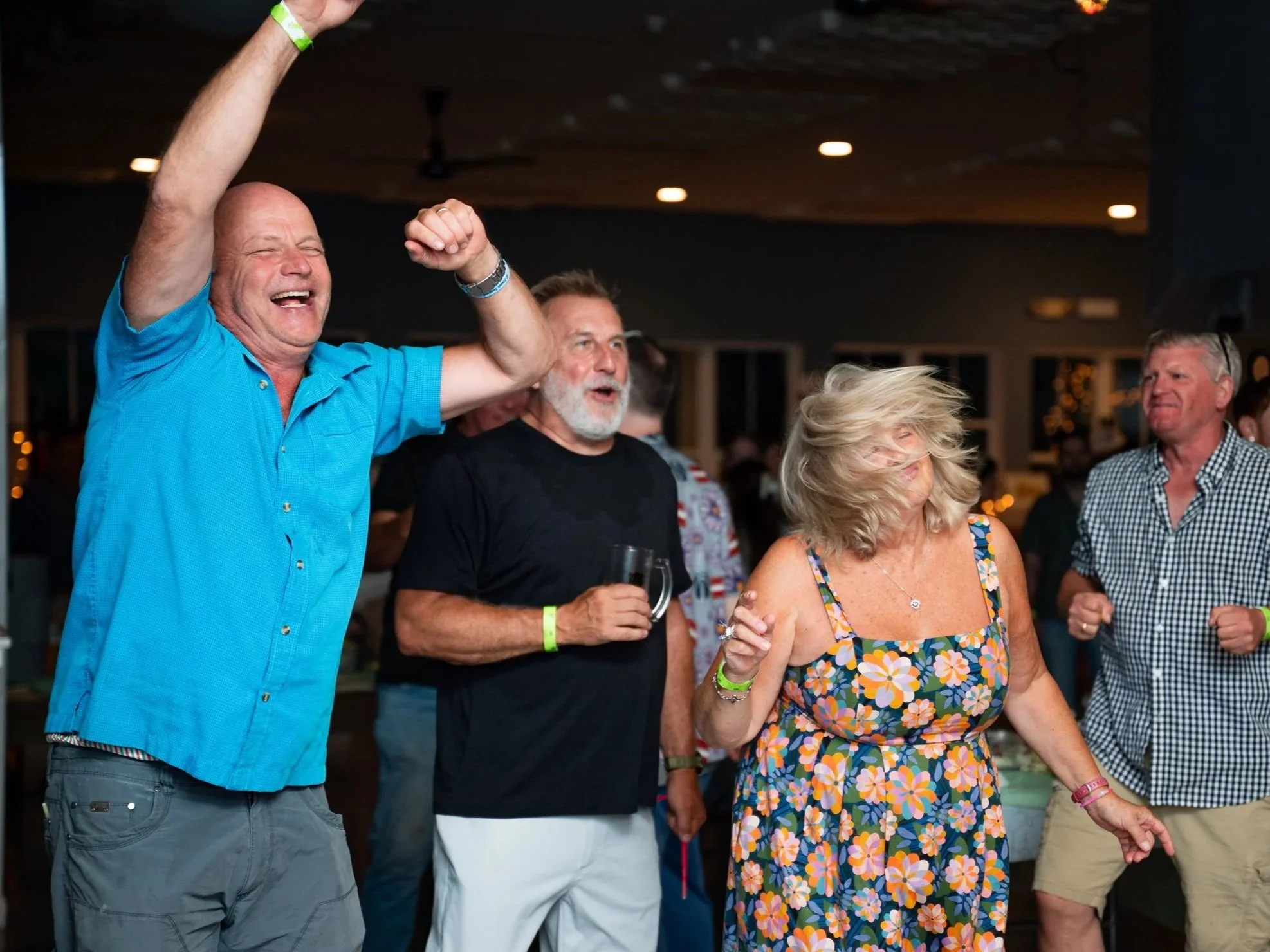 People dancing and enjoying themselves at a social event in a dimly lit indoor setting.