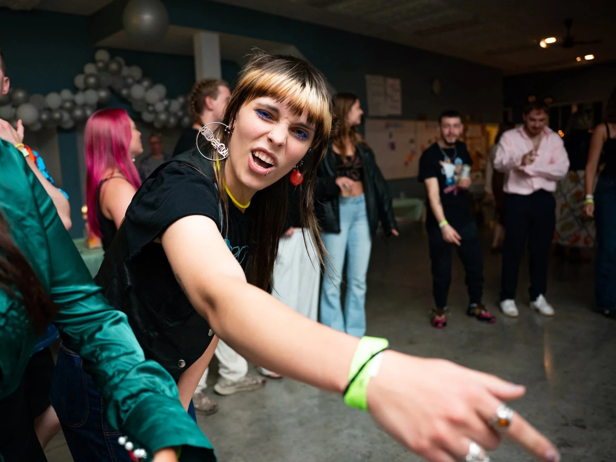 Group of young people dancing and having fun at a party or social gathering indoors, with balloons and decorations in the background.