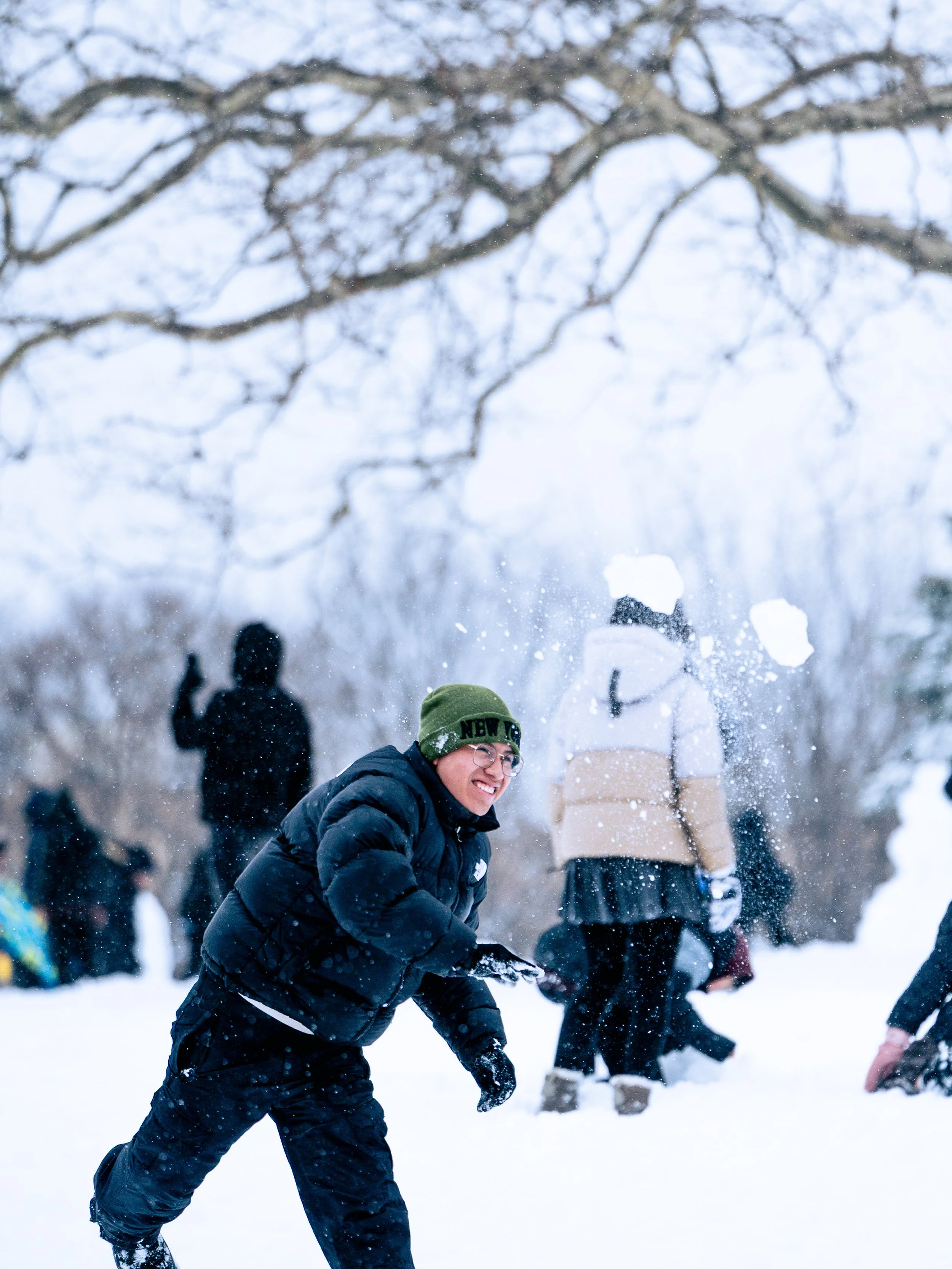 People playing and having fun in the snow, with a person in the foreground smiling and throwing snow in the air.
