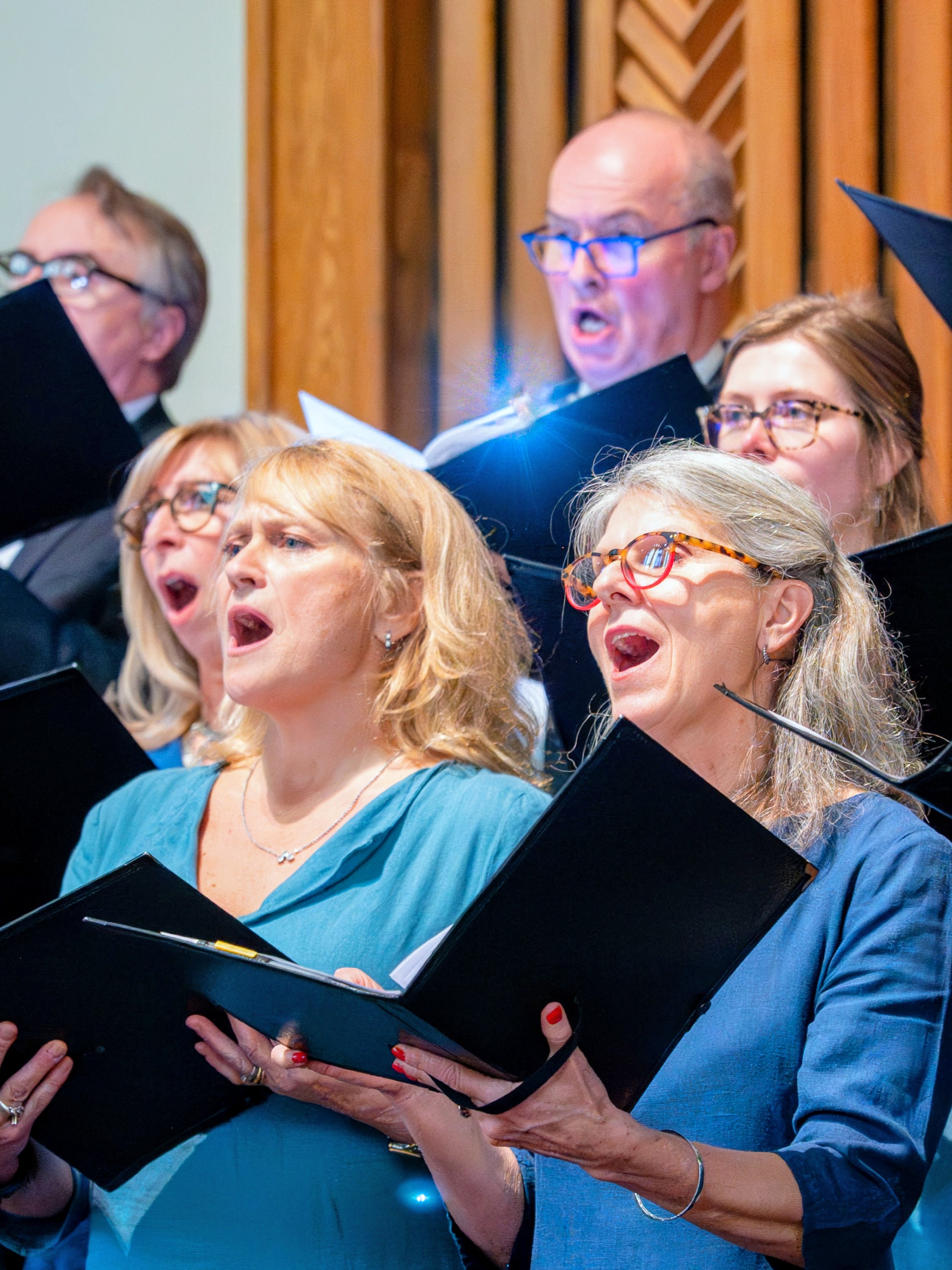 A group of people singing in a choir, holding sheet music, wearing graduation gowns and caps.