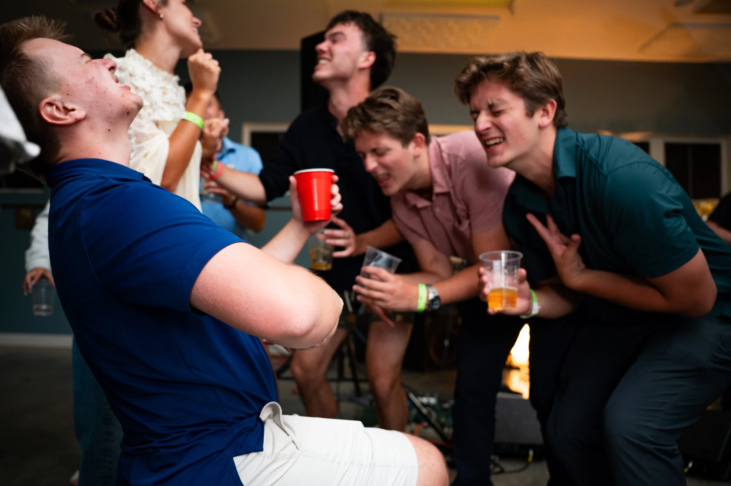 Group of young people at a party, laughter and dancing, holding drinks, having fun.