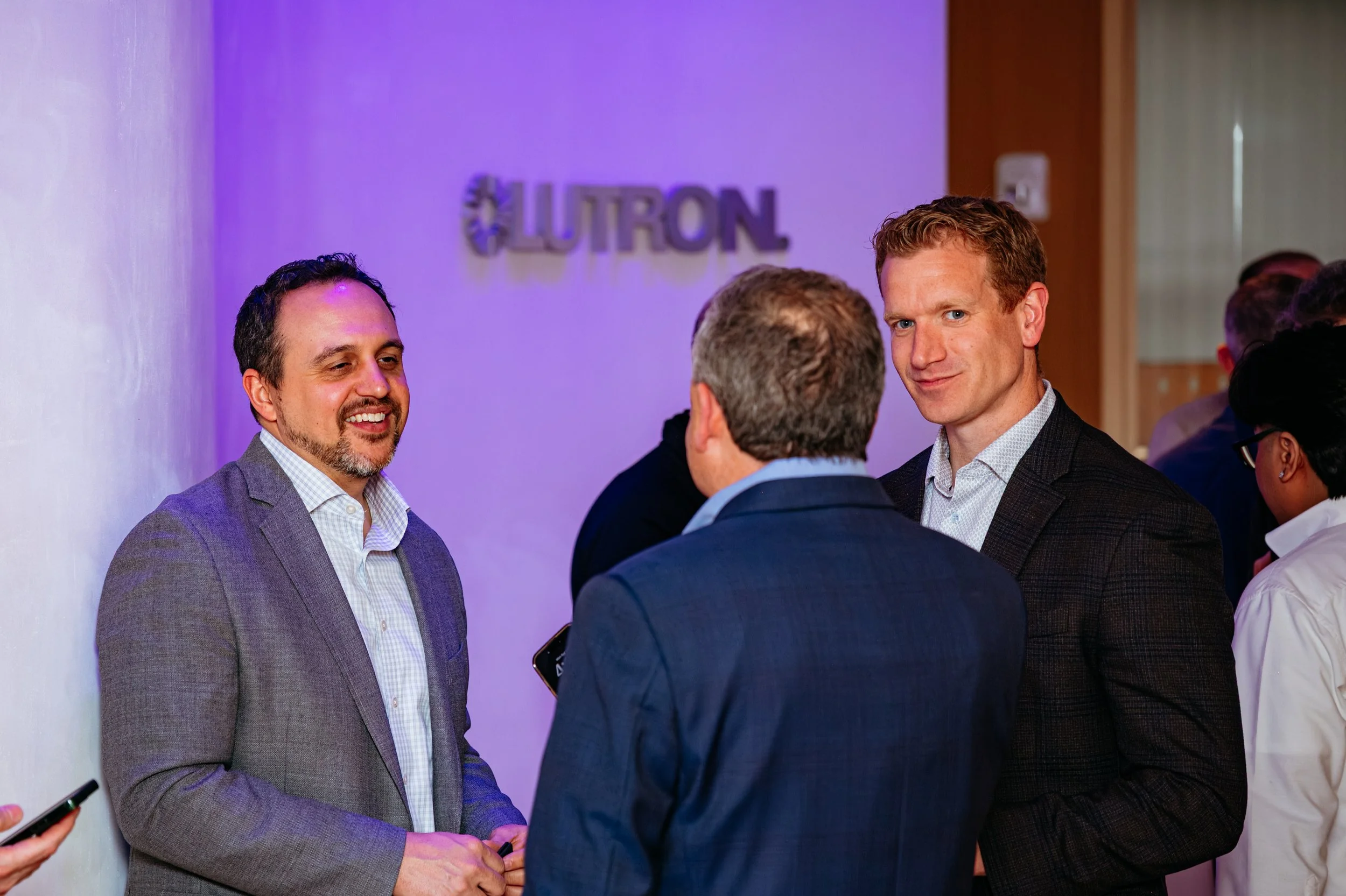 Several businesspeople engaged in conversation in a corporate setting with a Lutron sign on the wall in the background.