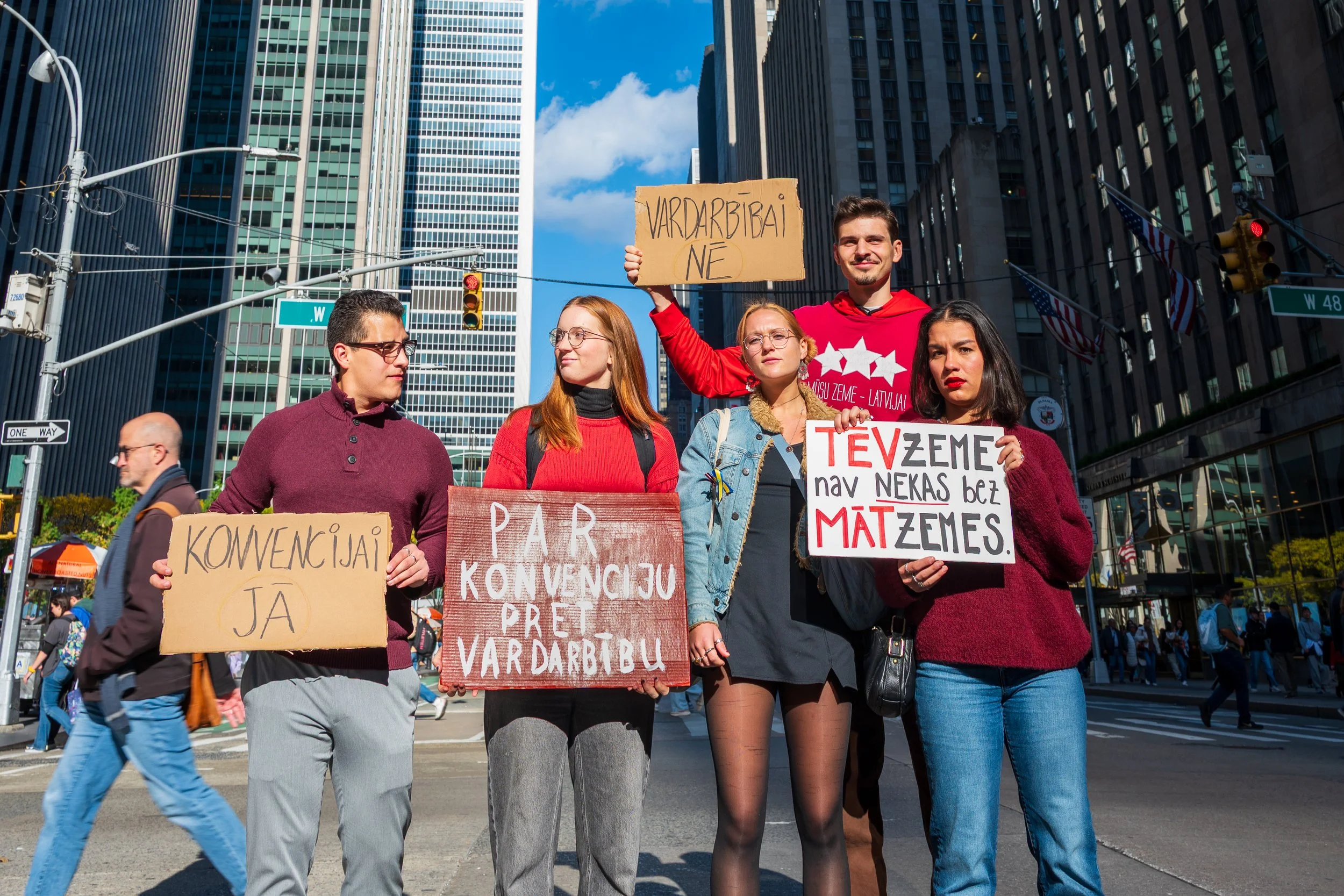 Group of people protesting on a city street holding signs in Latvian and English.