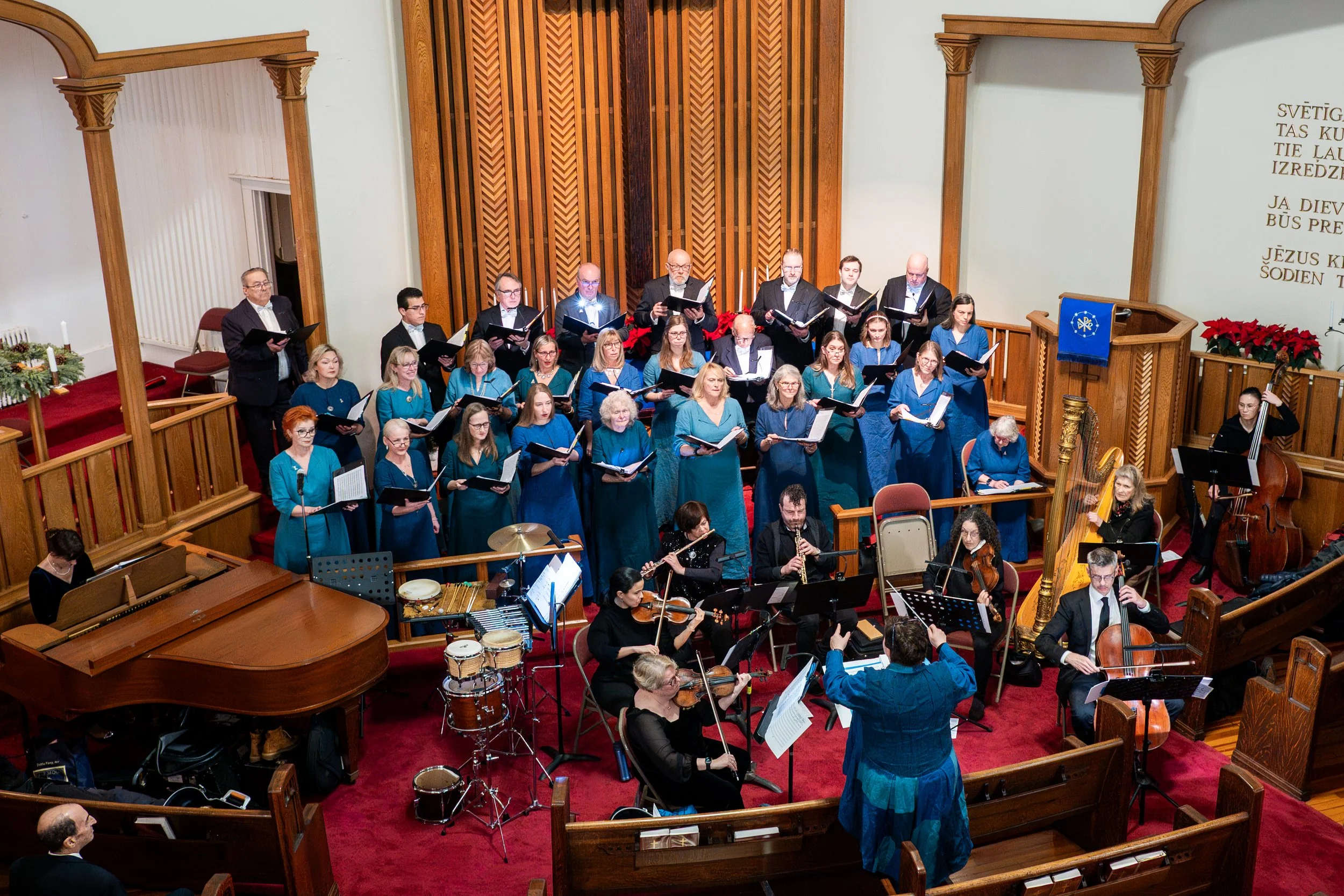 A choir and orchestra performing inside a church with wood paneling, Christmas decorations, and a large golden harp.