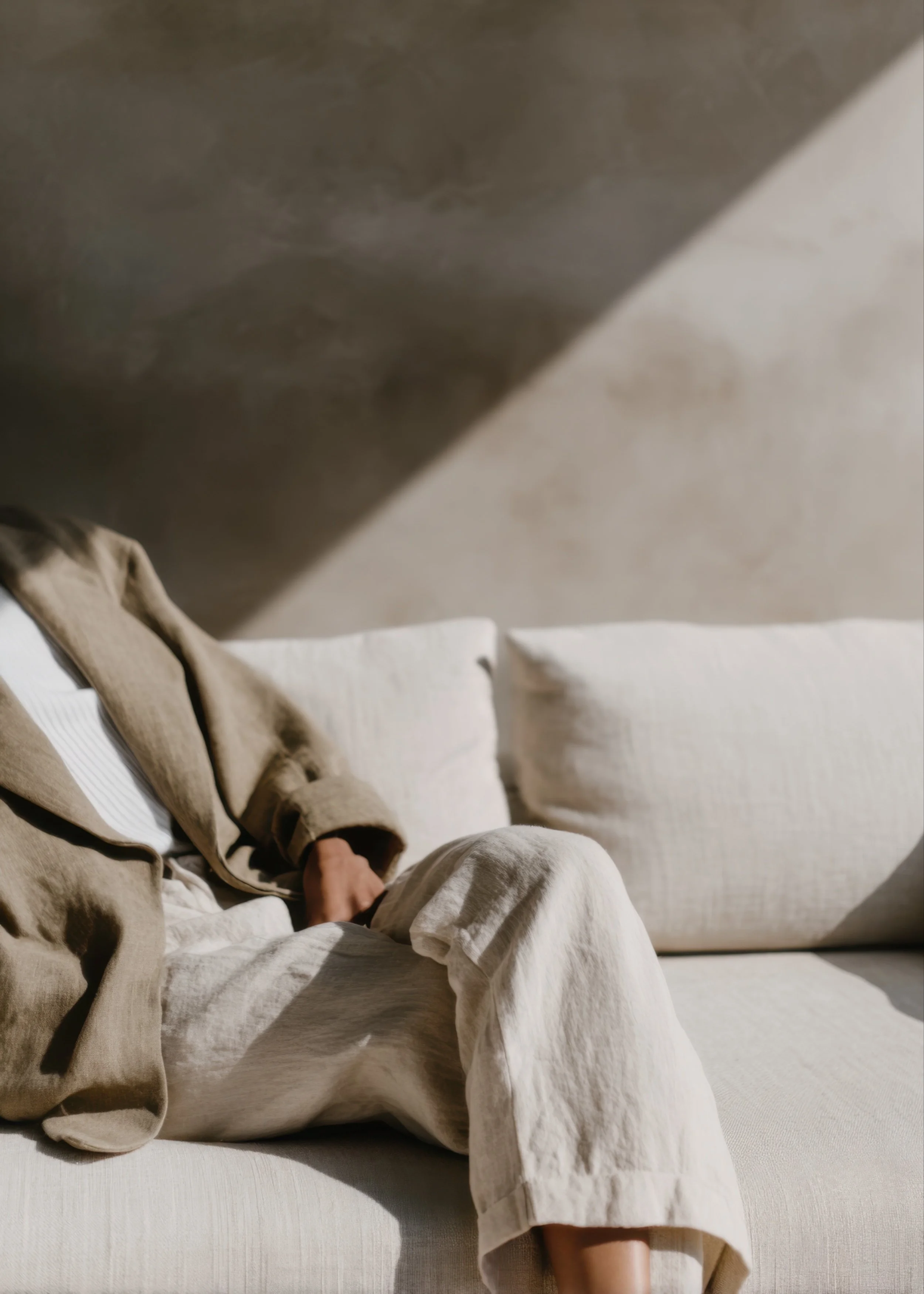 Person seated on a neutral sofa in sunlight wearing linen clothing with soft shadows and warm natural tones
