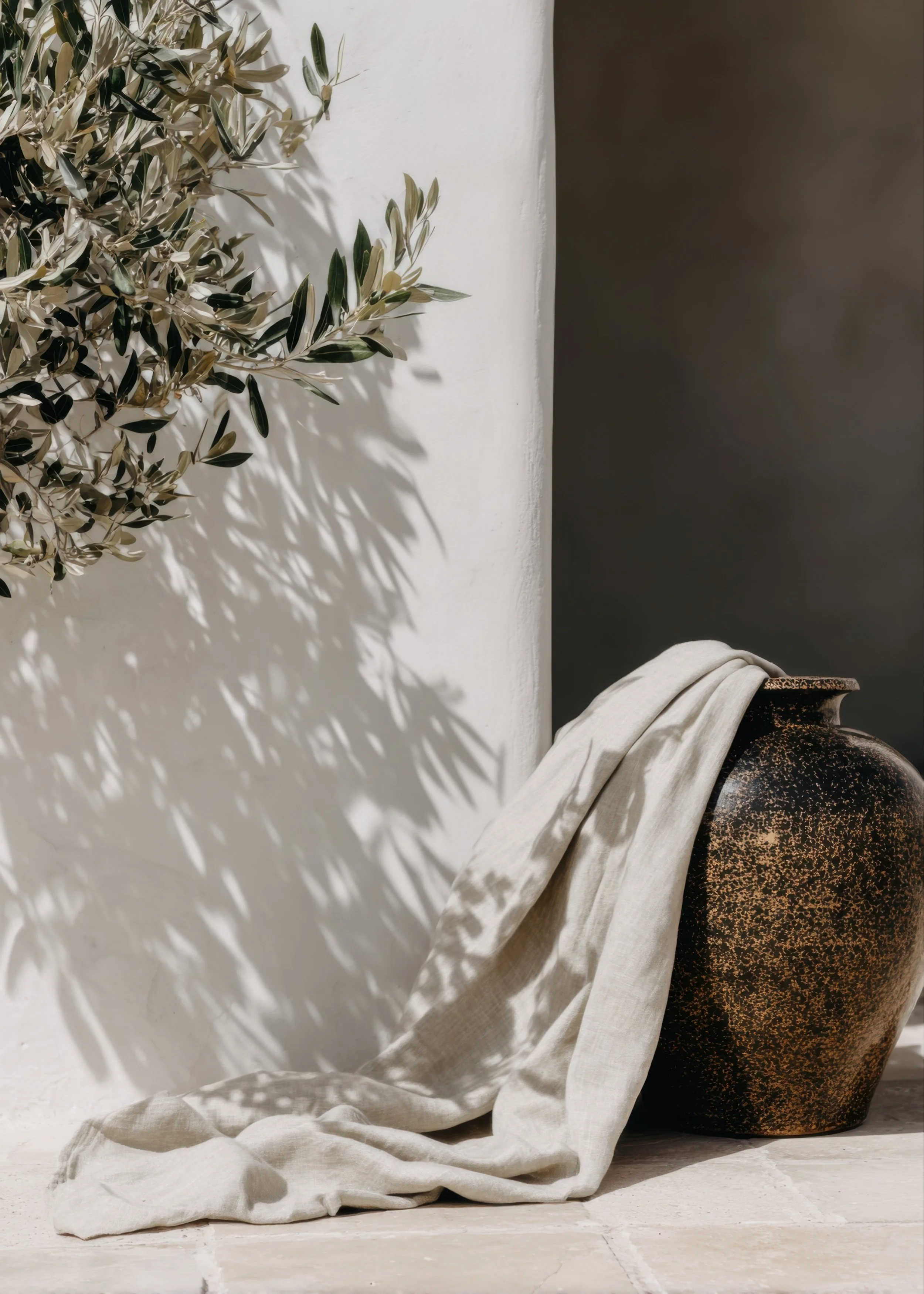 Olive branches, ceramic vase, and draped linen in soft natural light