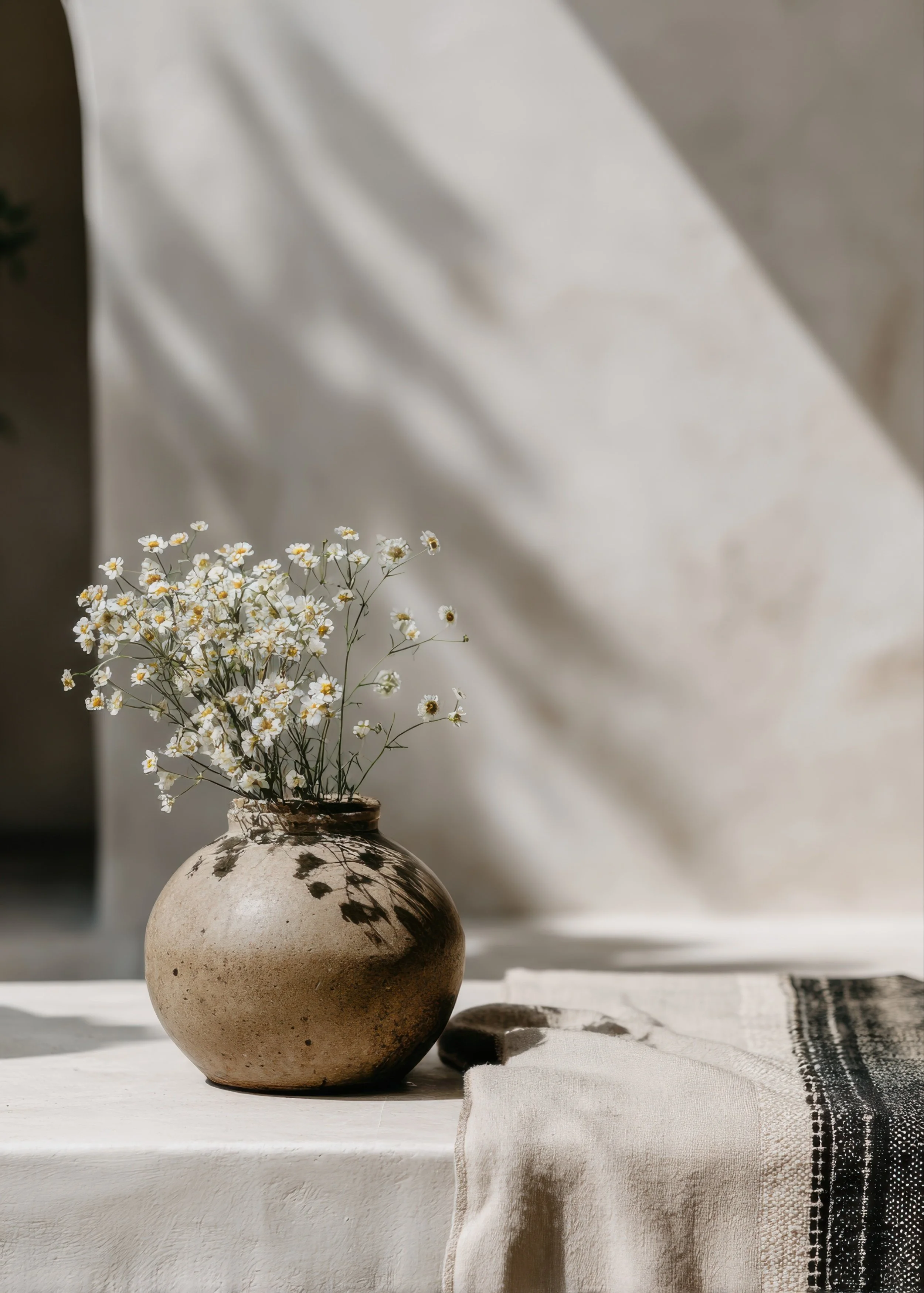 Neutral-toned interior with soft natural lighting, ceramic vase, and delicate flowers creating a calm, grounding, and restorative therapy-inspired environment