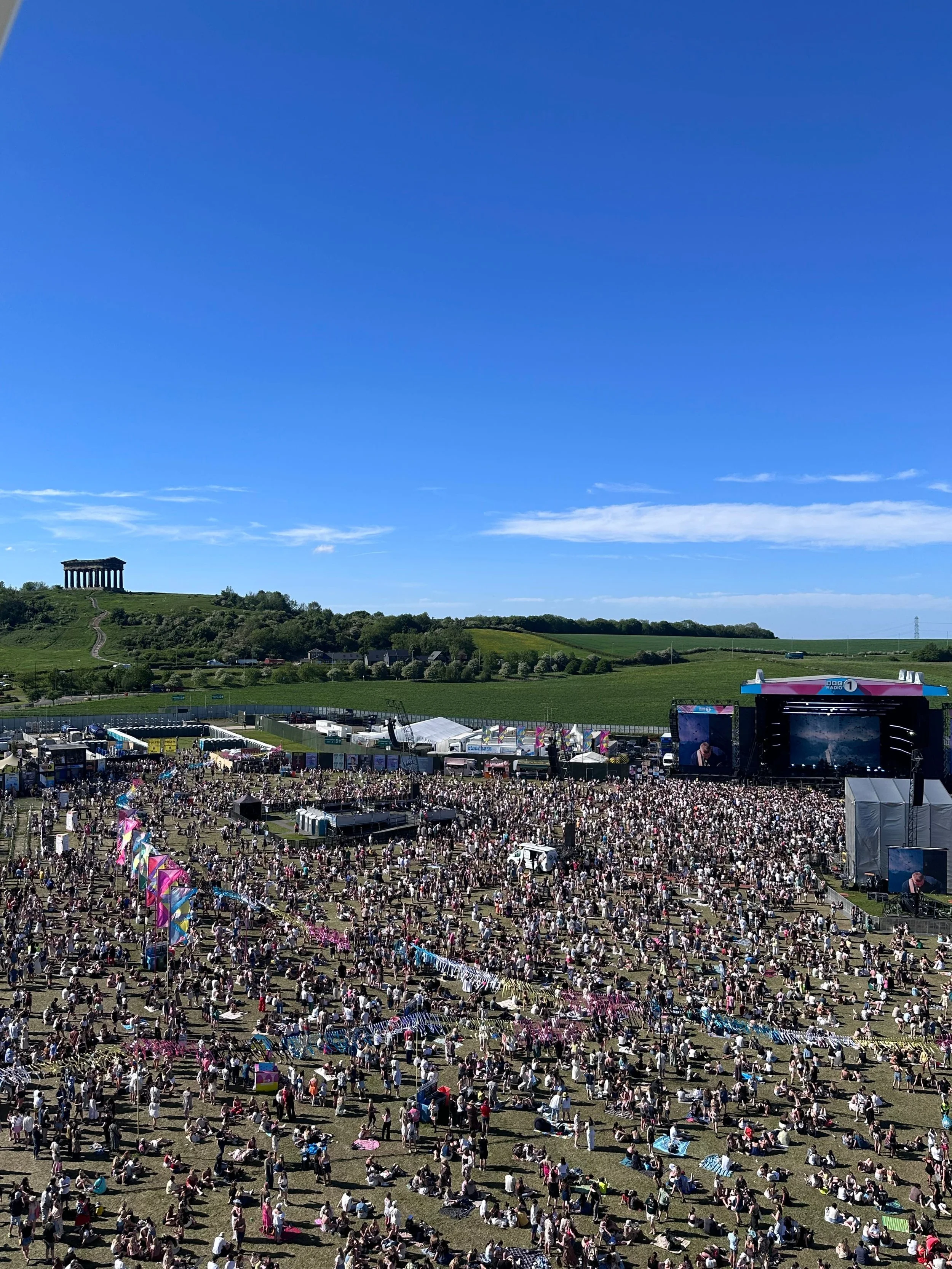 A vibrant crowd of festival-goers enjoying live music under a clear sky at a lively music festival.