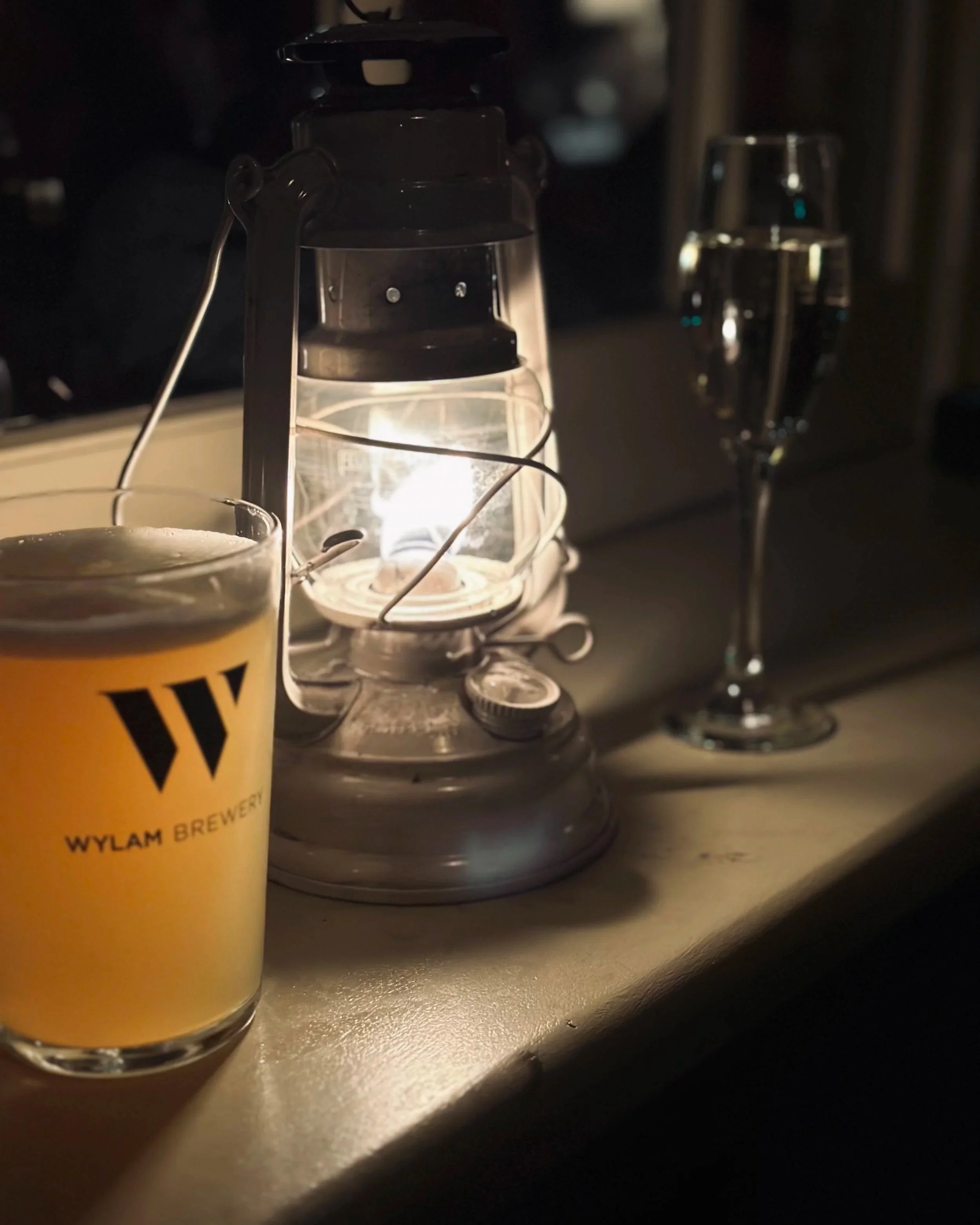 A dimly-lit lantern sitting inbetween a pint of beer and a glass of prosecco.