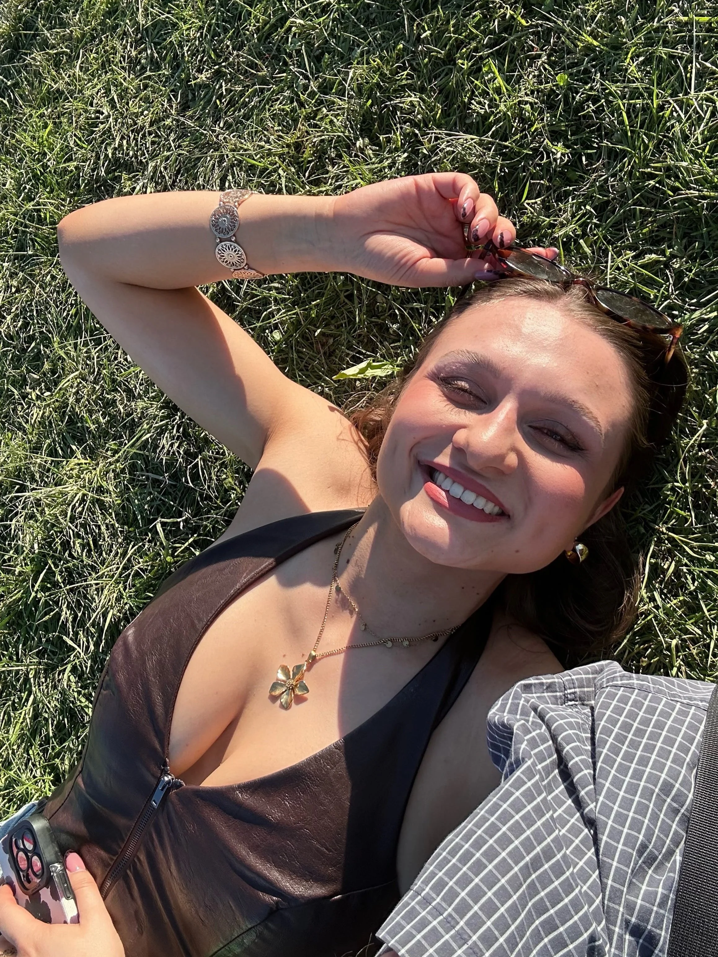 Young woman lying on green grass in bright sunlight, smiling with eyes closed at an outdoor summer festival.