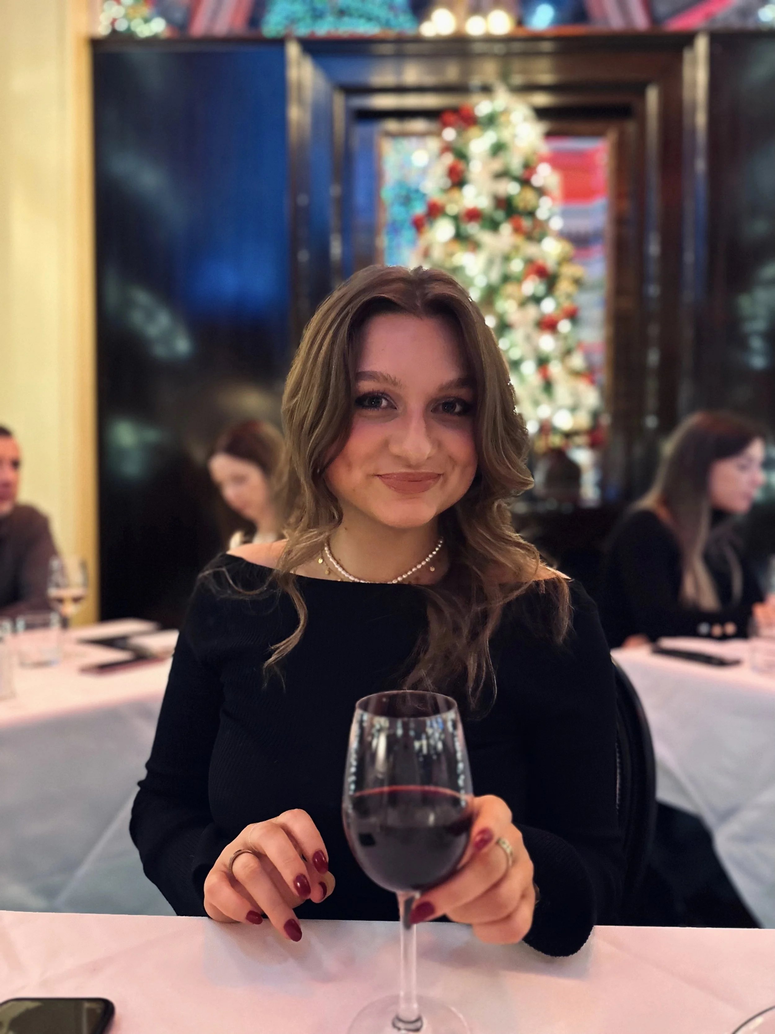 A woman sitting in the restaurant at the Dome, Edinburgh, holding a glass of wine with Christmas decorations behind her