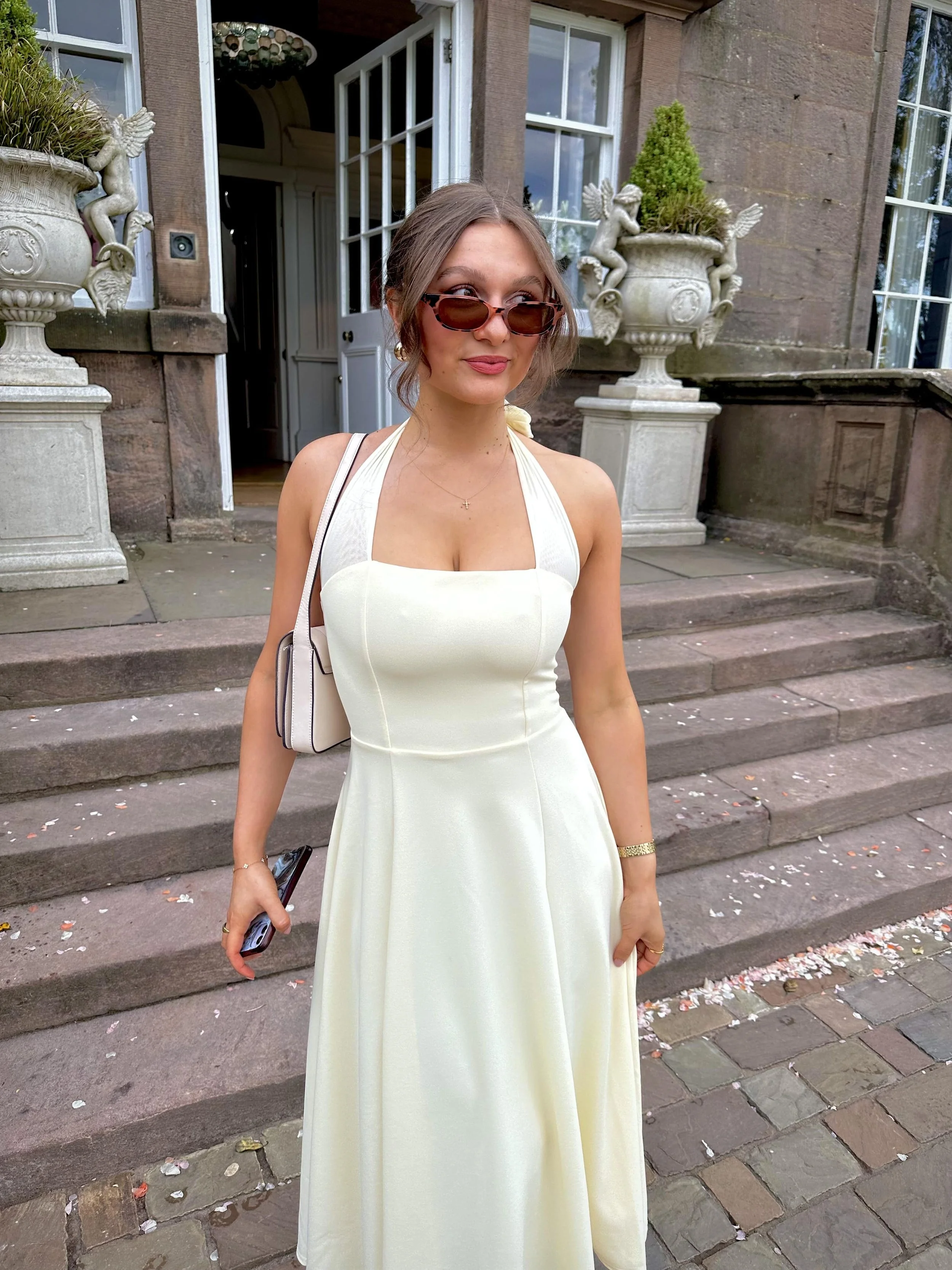 A woman in a yellow dress wearing sunglasses in front of a wedding venue