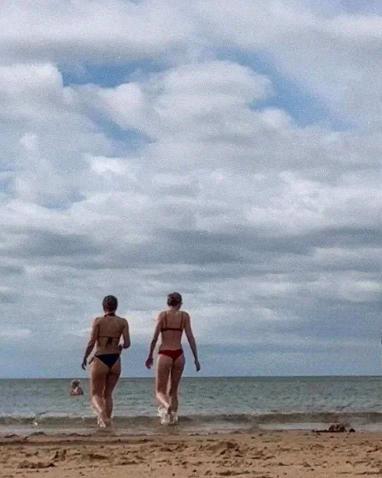 Two friends sit on the sandy beach, sporting stylish sunglasses and soaking up the sun.