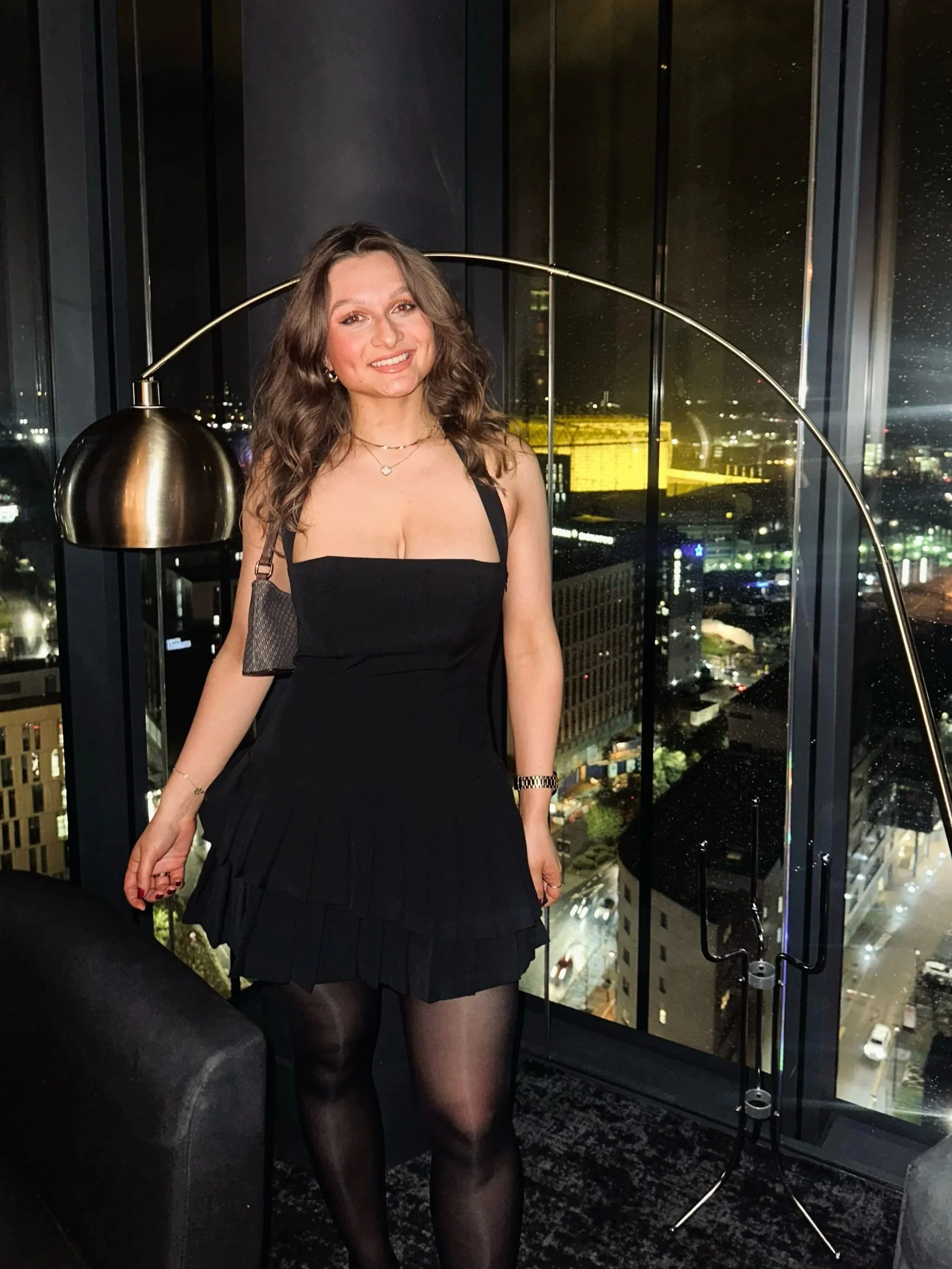 Woman standing in front of window wearing an Oh Polly Black Pleated Dress 'Rosaria'