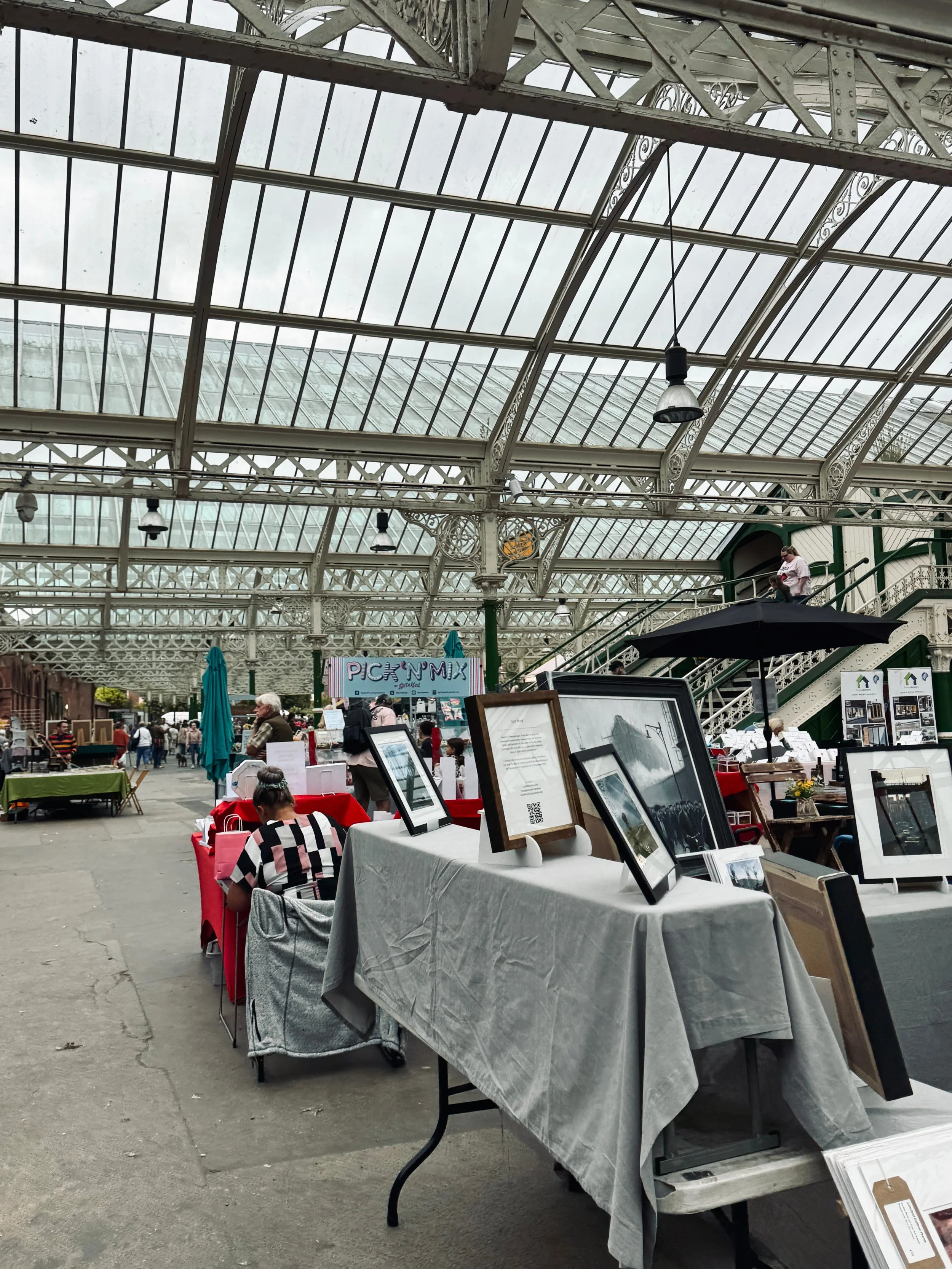 A bustling indoor market featuring tables and chairs, filled with vendors and shoppers enjoying the vibrant atmosphere.