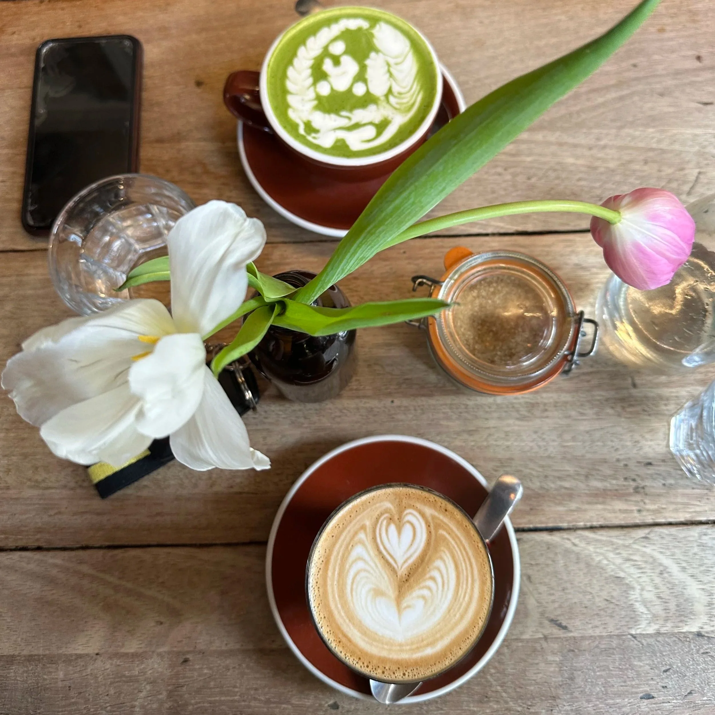 A table with a cup of matcha, a cup of coffee, and a decorative plant