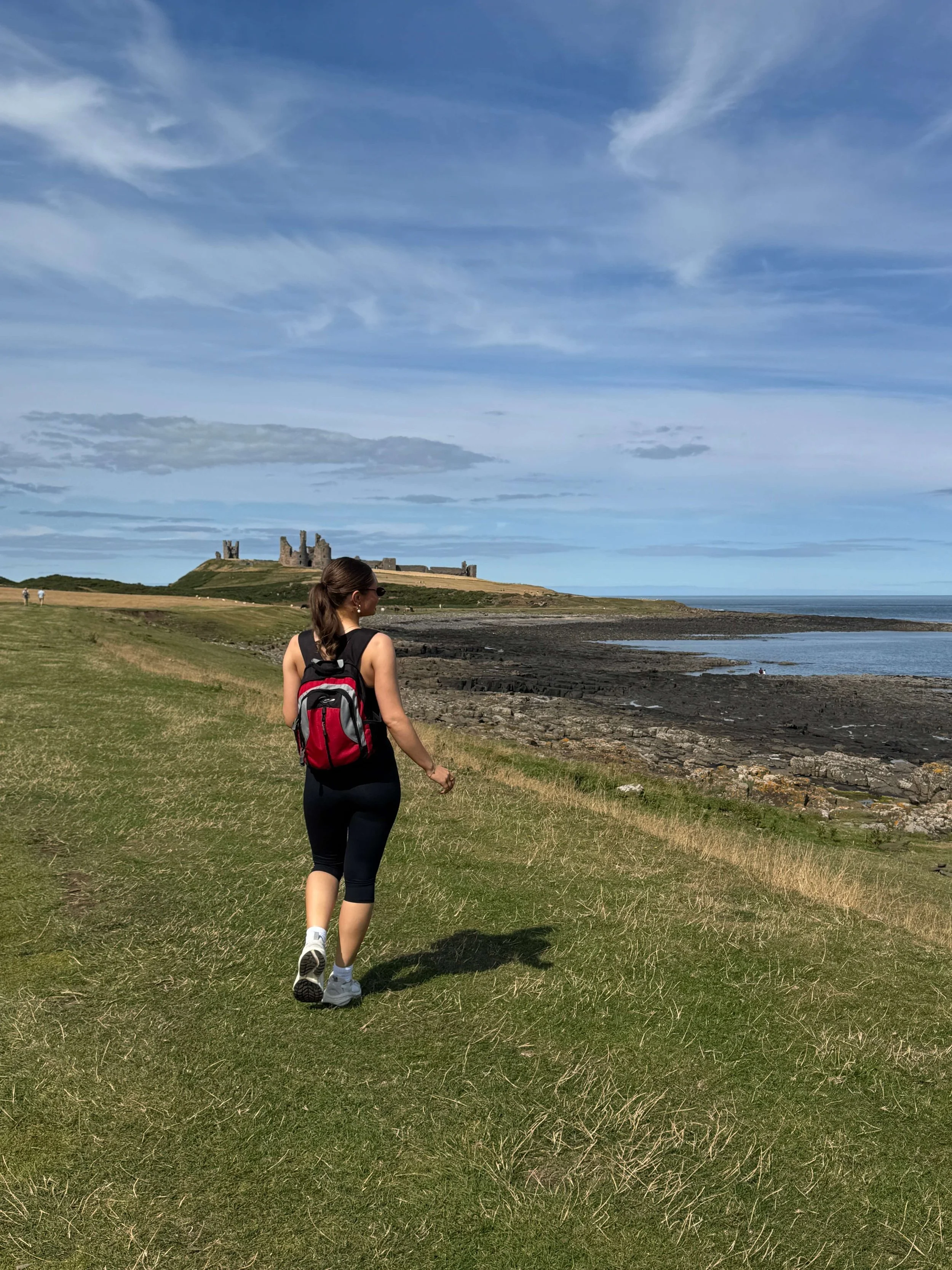 A woman in a black shirt and black shorts walking across a grassy field with a castle in the background.