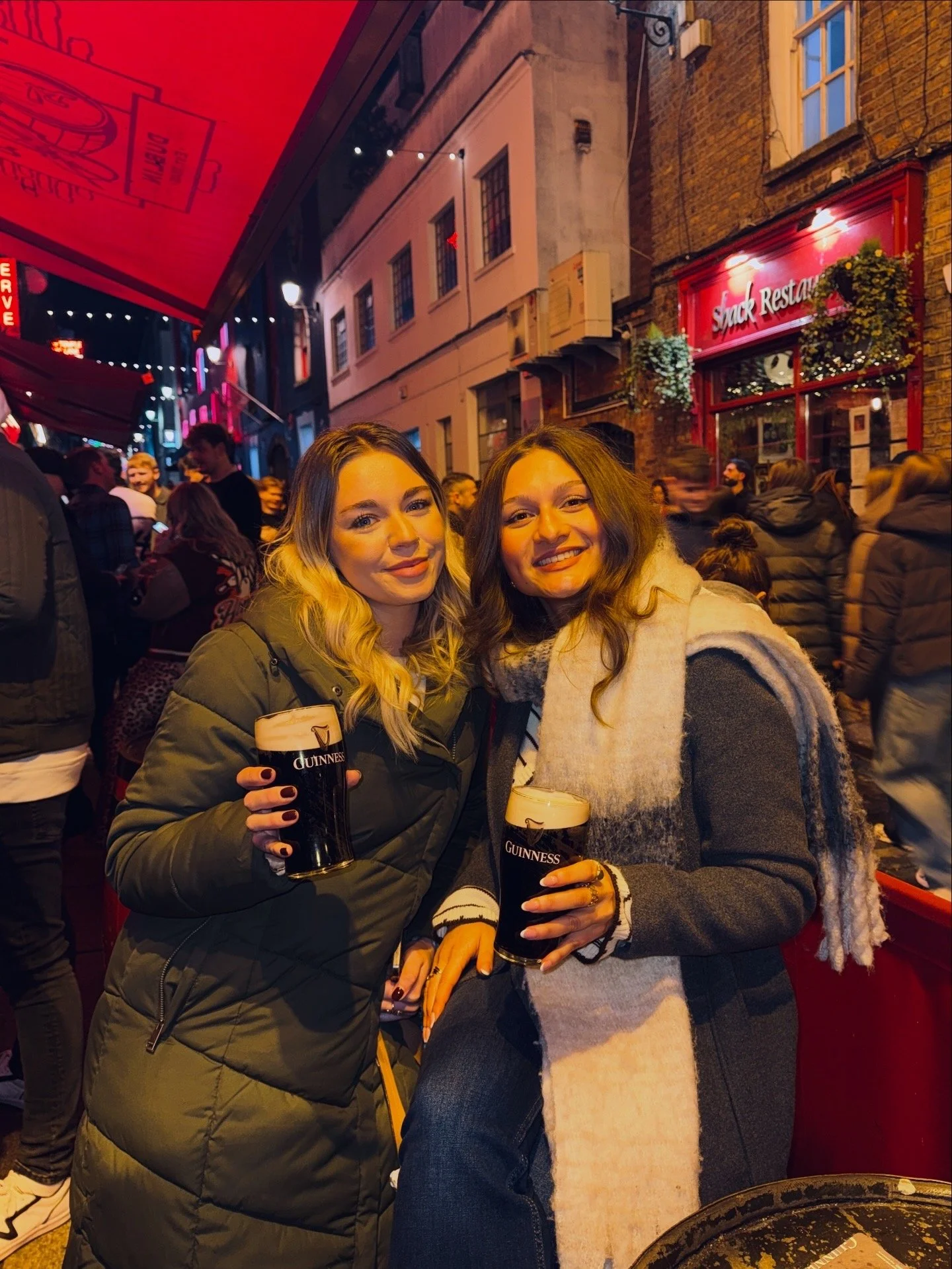 Two girls smiling and posing for a photo outside the Temple Bar in Dublin with a pint of Guiness