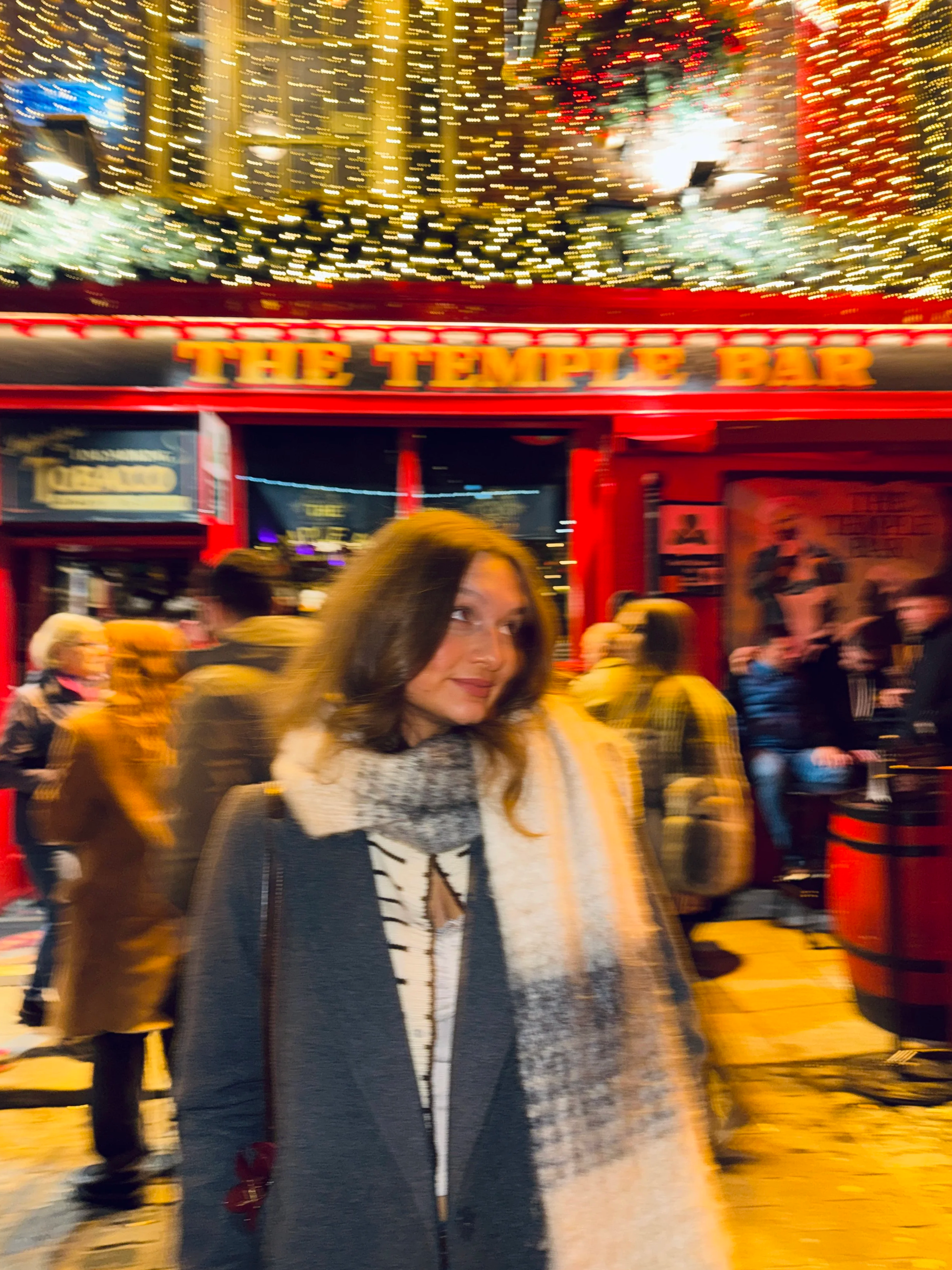 A woman standing outside the Temple Bar in Dublin, wearing a coat and scarf at Christmas time
