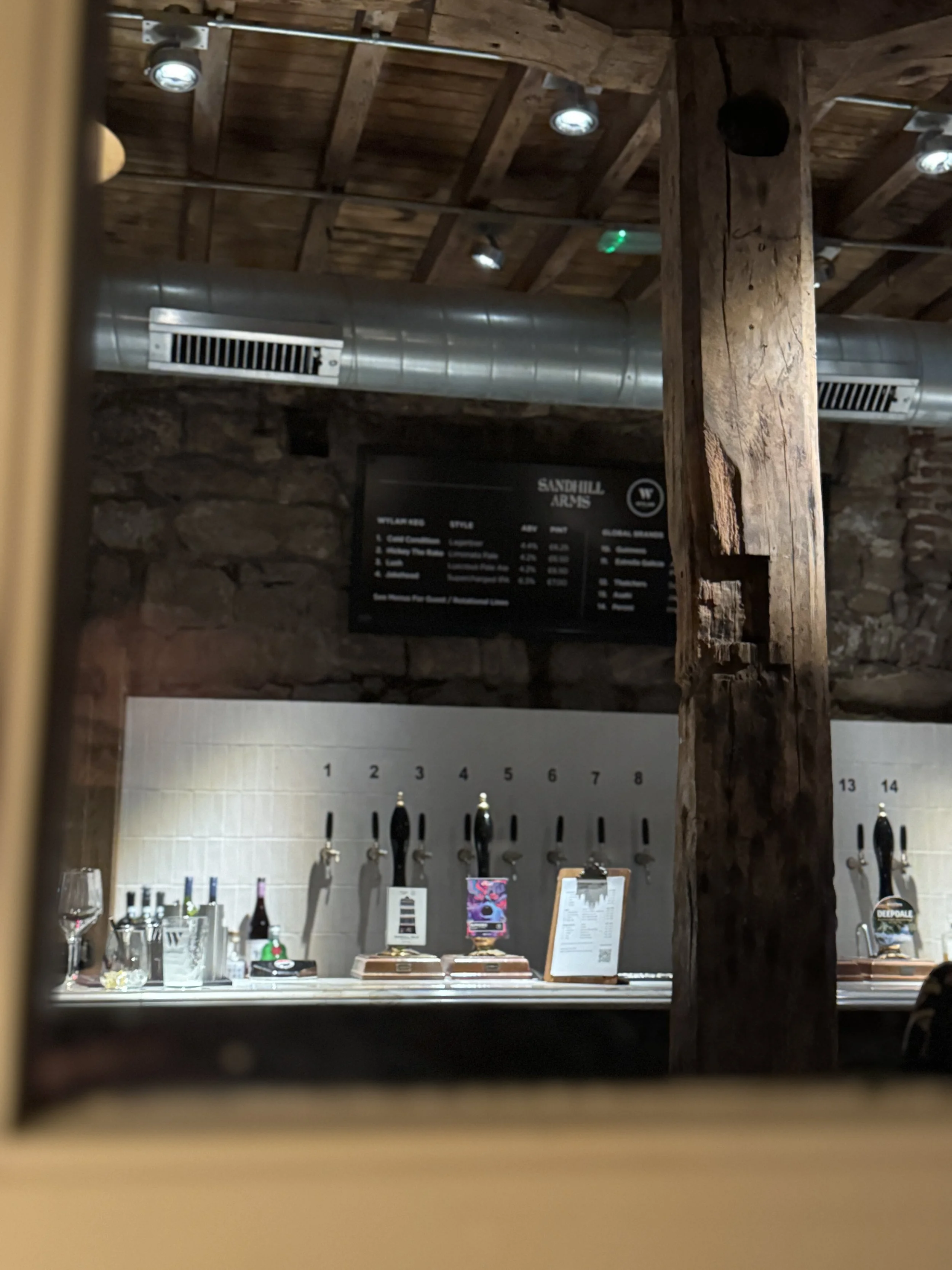 A shot of a bar through a window, showing beer taps, a menu, and the wooden beam of the interior