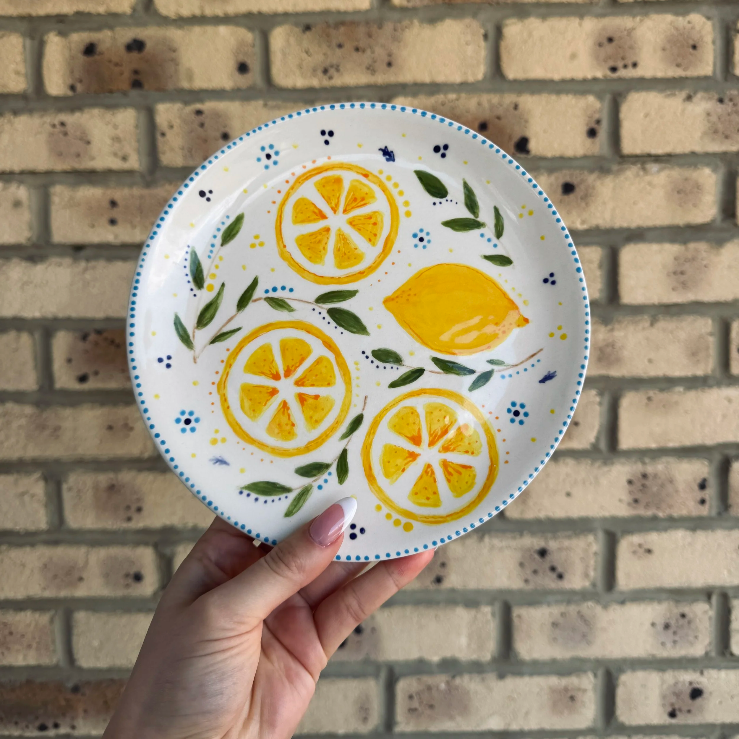 A hand holding a hand painted plate with a lemon design