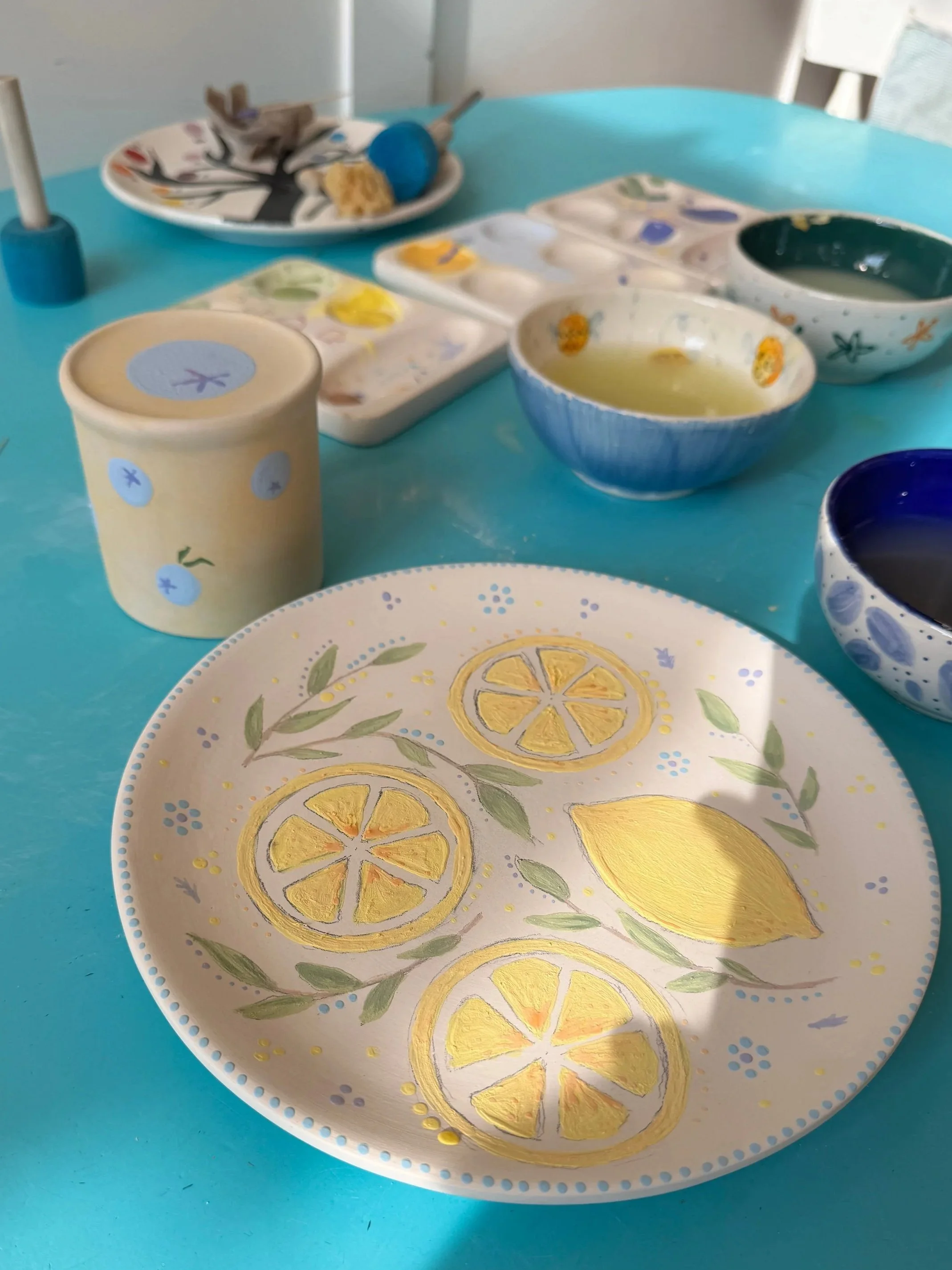 A painted plate and mug, with paints and brushes in the background