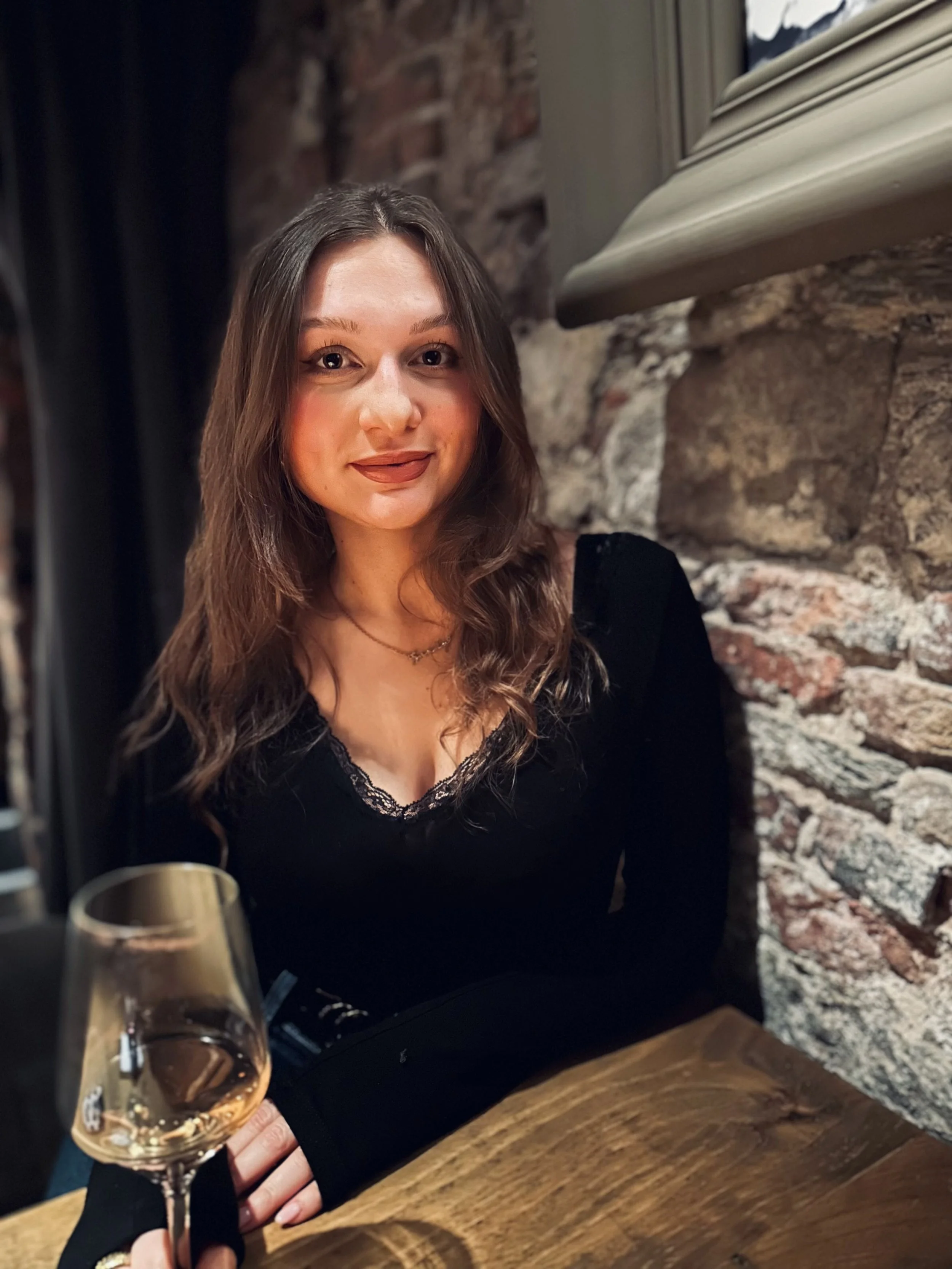 A woman sitting in front of an exposed brick wall in a pub with a glass of wine