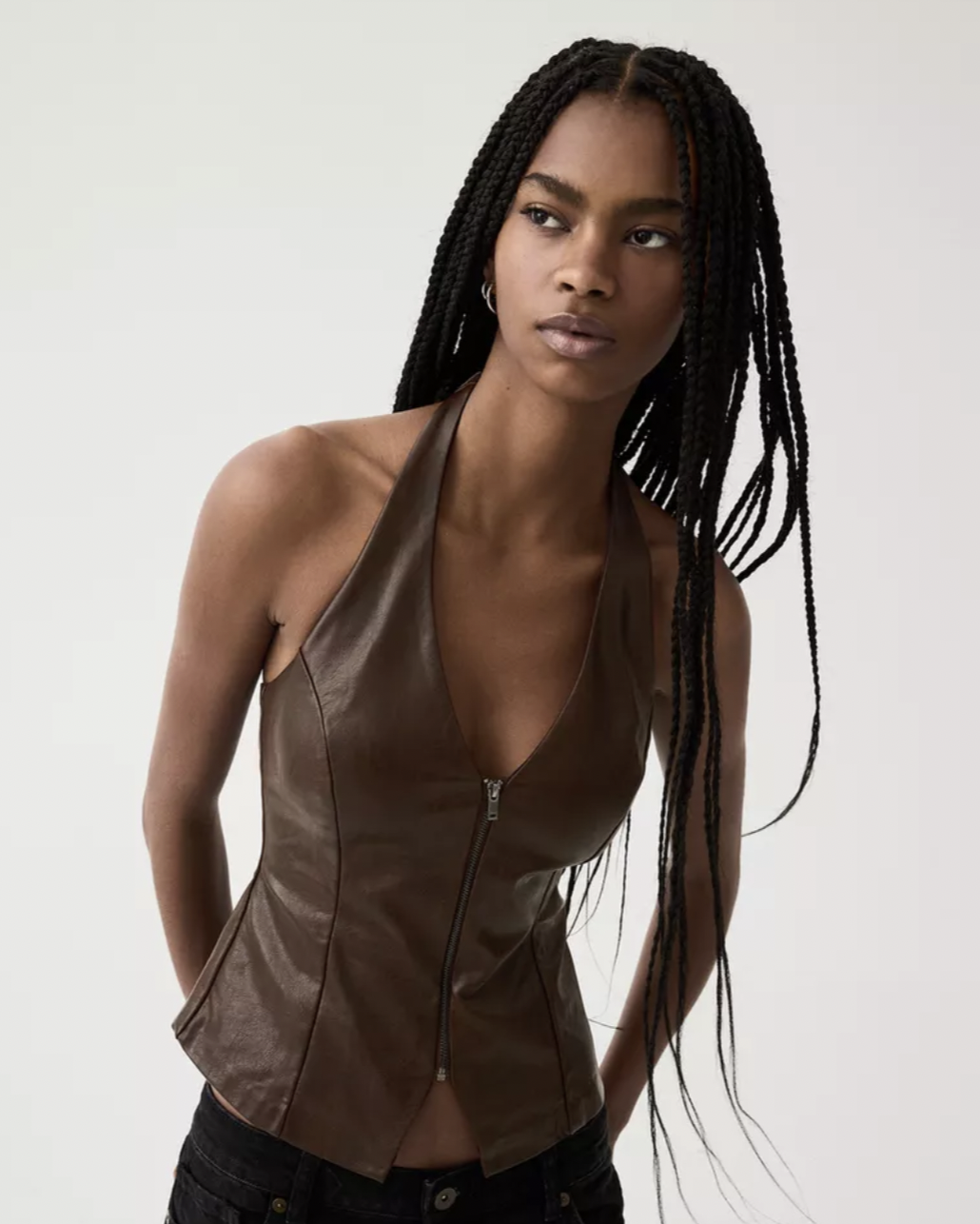 Woman wearing a sleeveless brown leather halter top with a front zipper and black pants, posing against a plain white background.