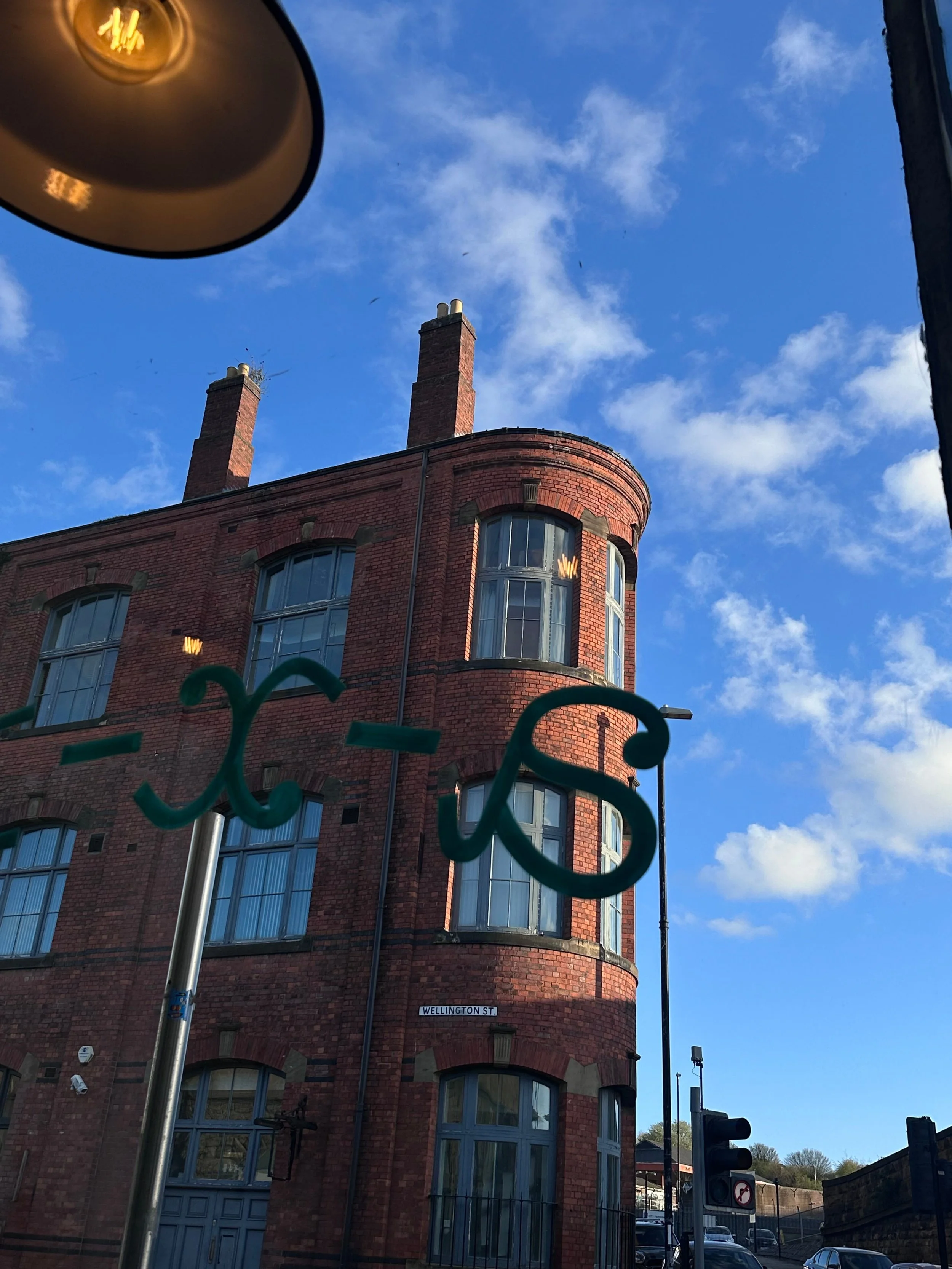 View through a window of a vintage red brick building under a bright blue sky. A round, lit ceiling lamp is partially visible in the upper left corner.