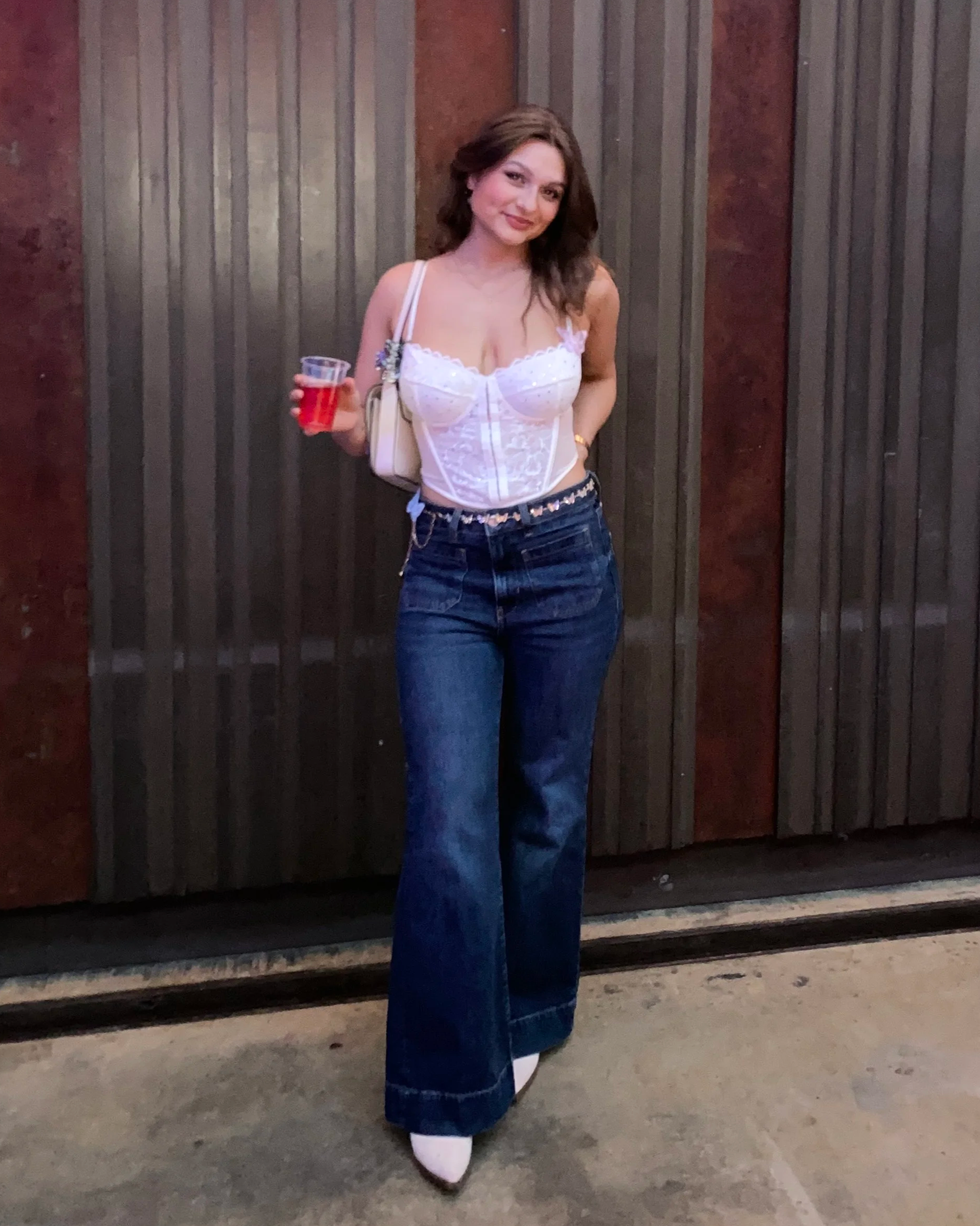 A woman holding a drink and wearing blue bootcut jeans and a white top