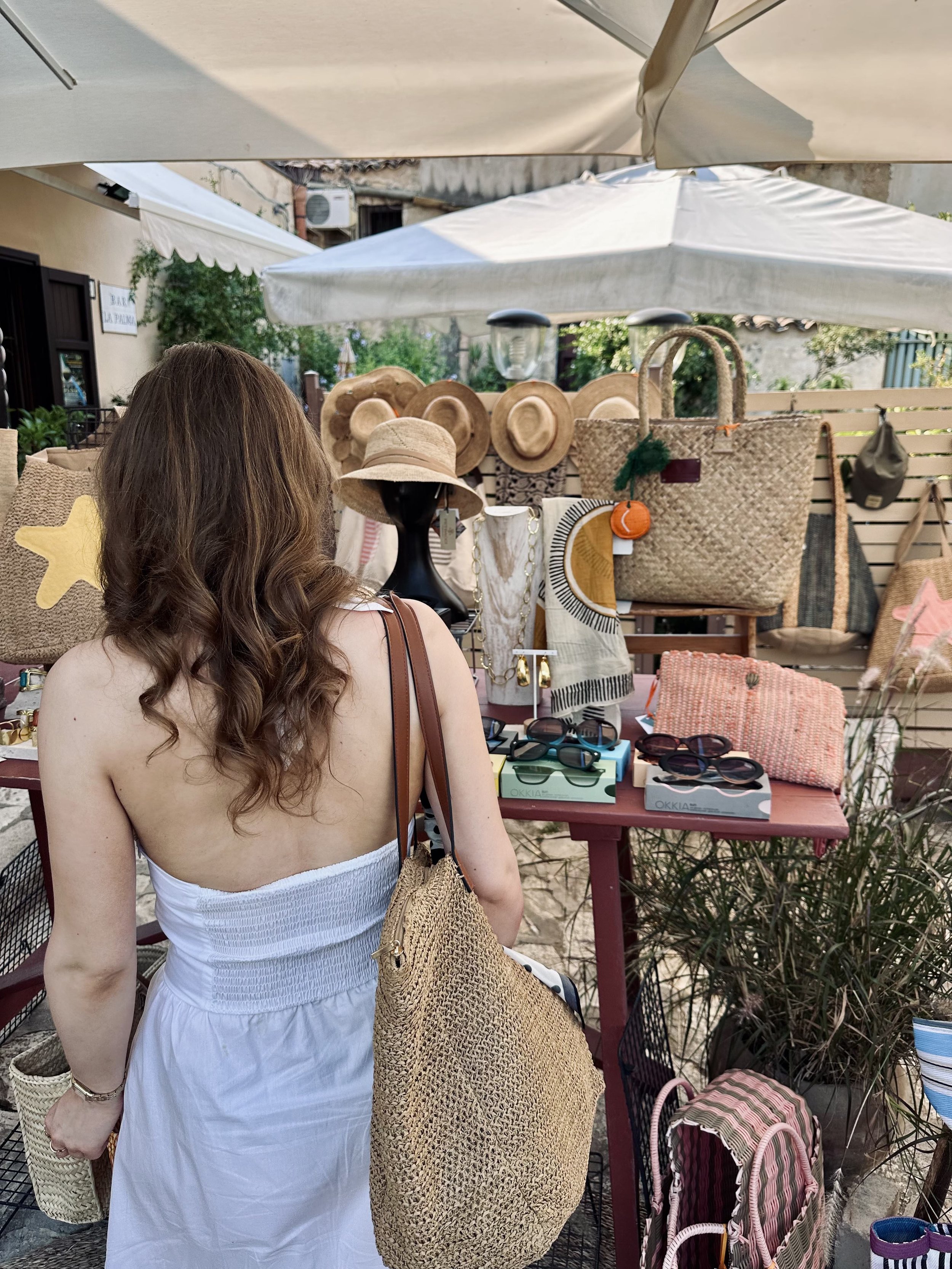 A woman in a flowing white dress studies a table adorned with colorful bags.