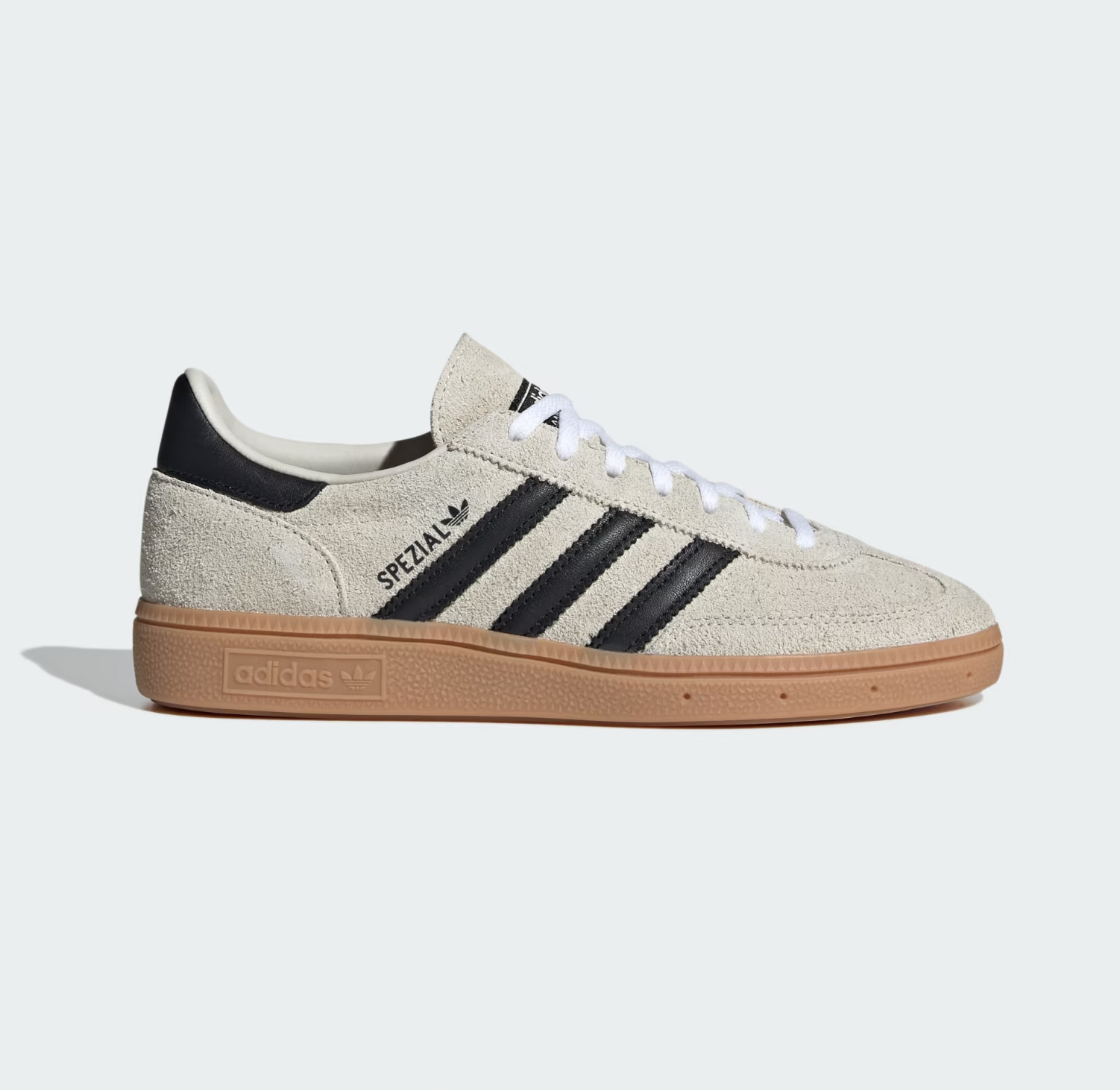 Cream suede Adidas sneaker with black stripes and "Spezial" text, featuring white laces and a brown rubber sole, against a light gray background.
