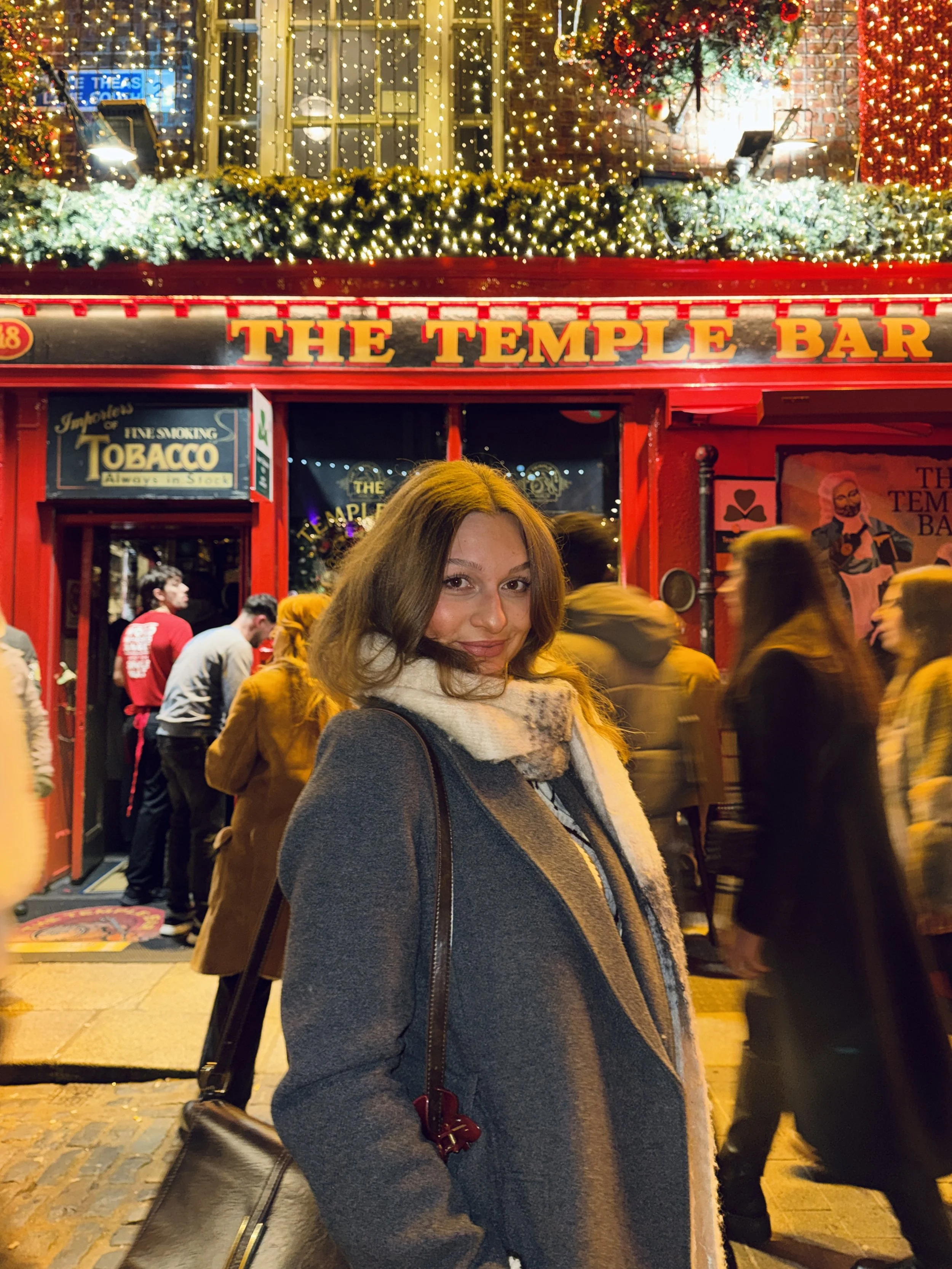 A woman in a long coat standing outside the Temple Bar in Dublin at Christmas time