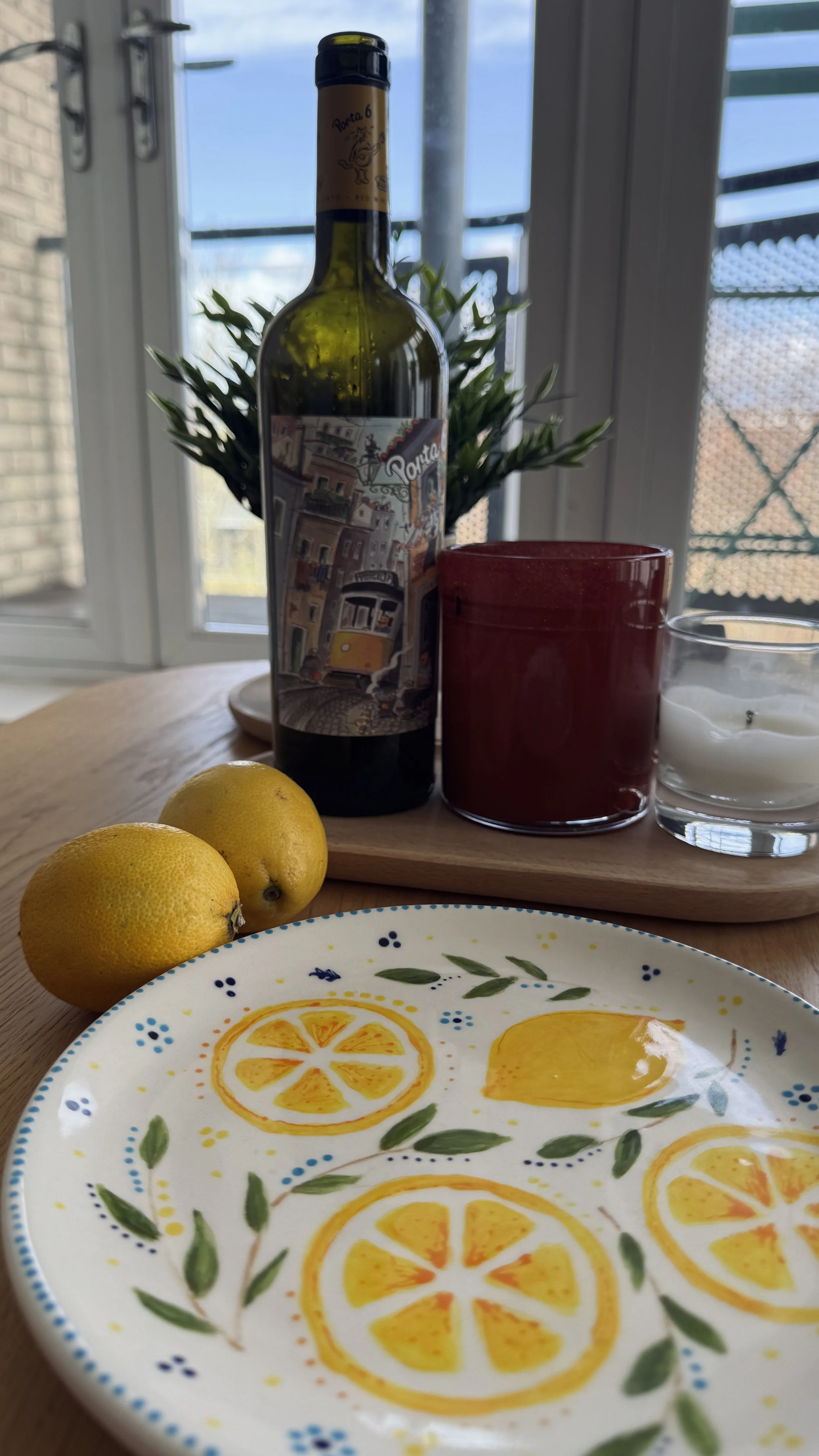 A hand painted lemon plate with lemons in the background, candles, and a wine bottle.