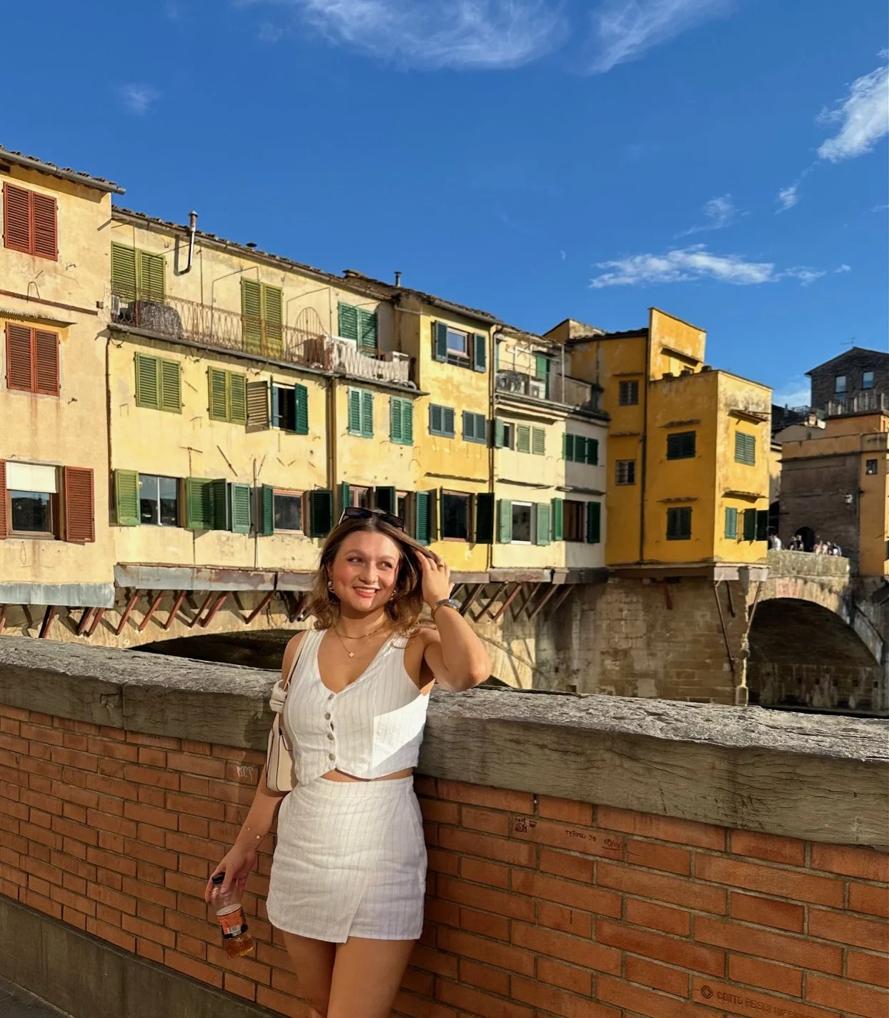 A woman standing in front of the Ponte Vecchio in Florence wearing sunglasses and a linen two piece