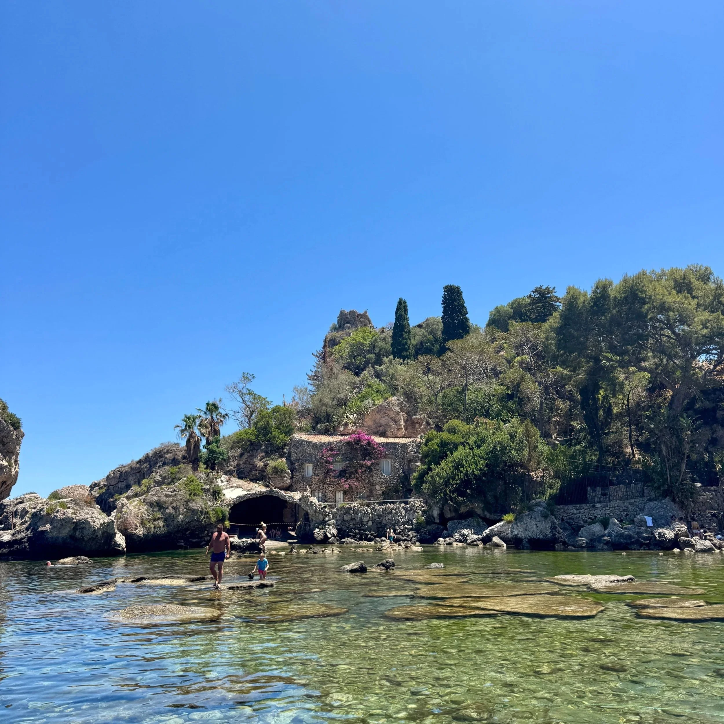 A group of swimmers enjoys the clear water near a rocky island, surrounded by vibrant blue skies and serene nature.