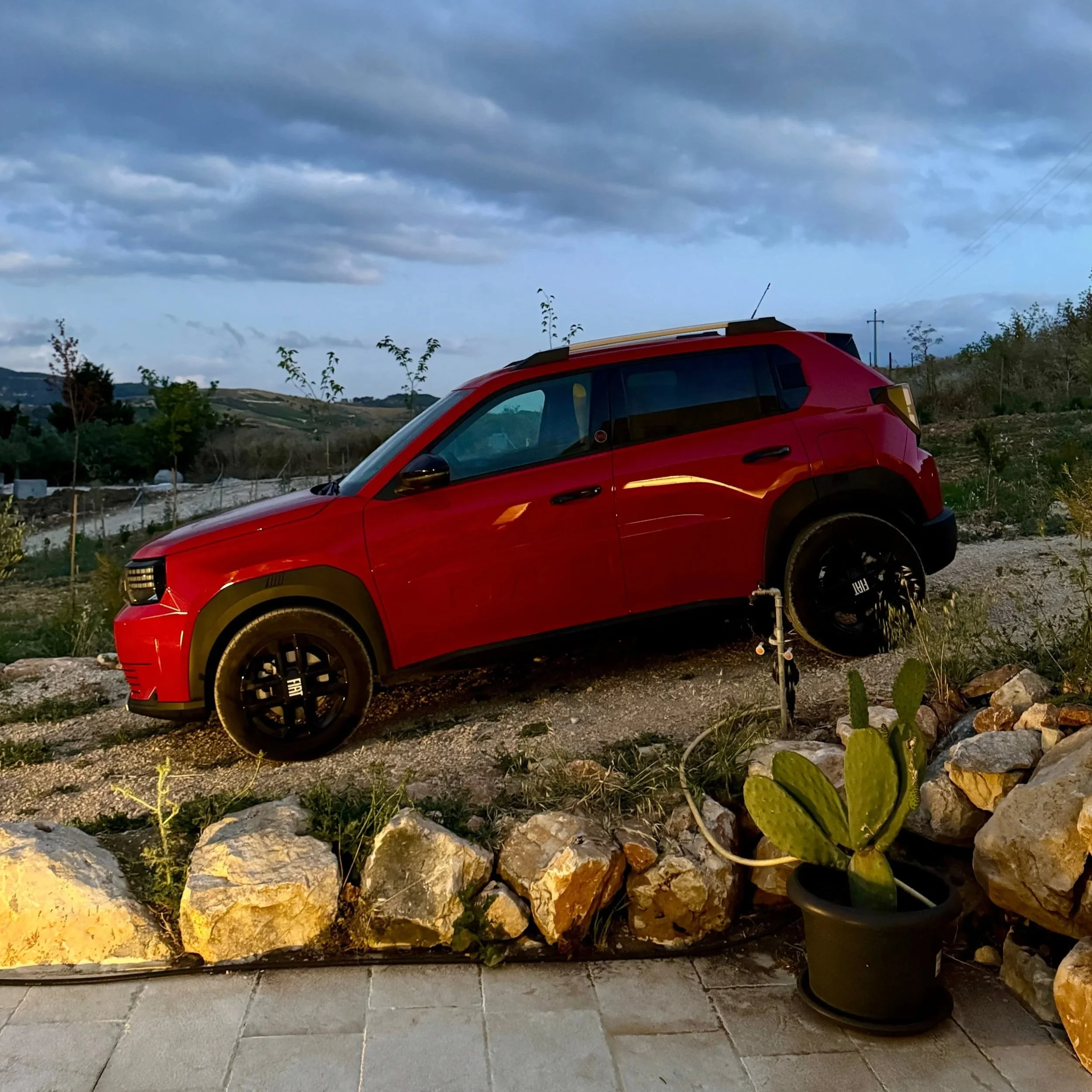 A vibrant red car parked on a rugged rocky hillside, surrounded by natural scenery.