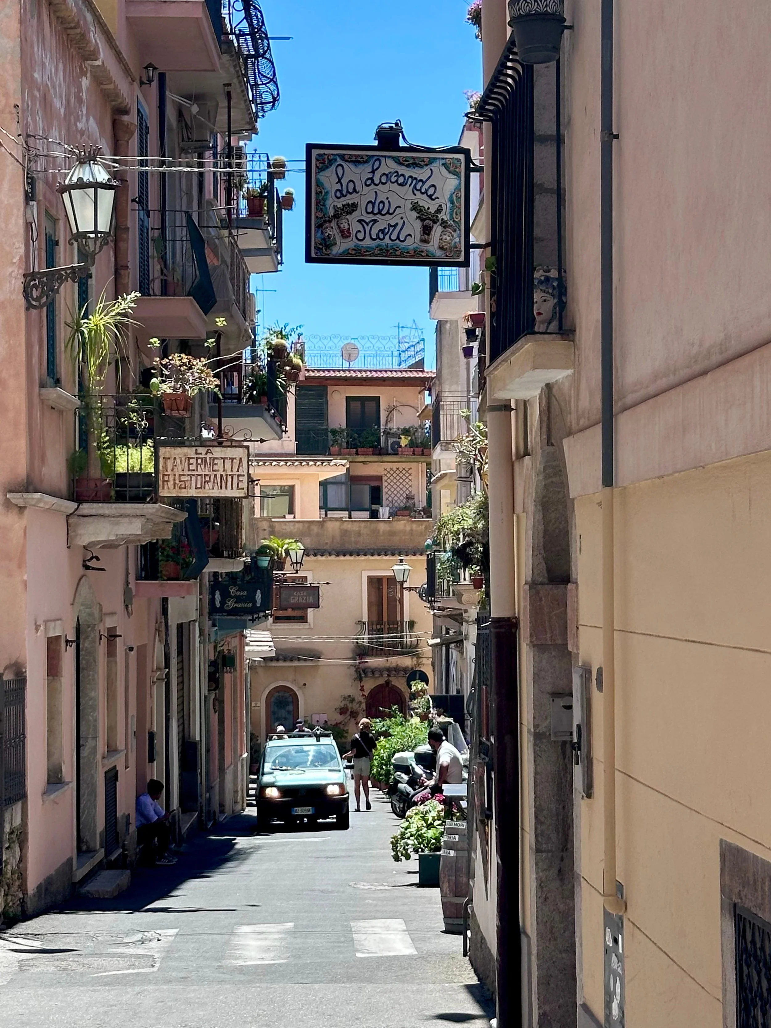 A bustling narrow street with vehicles parked along both sides, showcasing the vibrant urban environment.