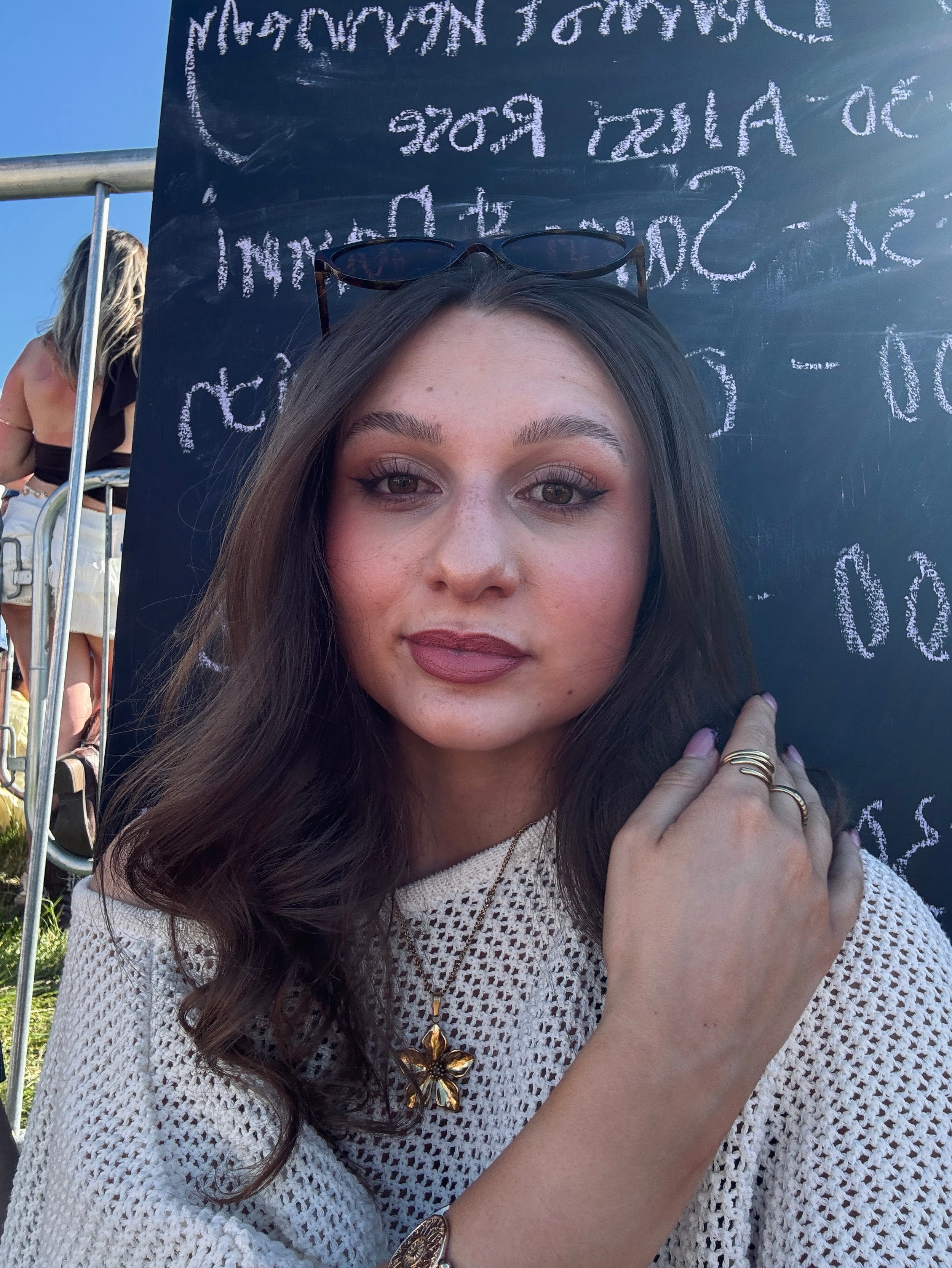 Close-up portrait of a young woman with long wavy brunette hair posing outdoors at a summer festival or event.