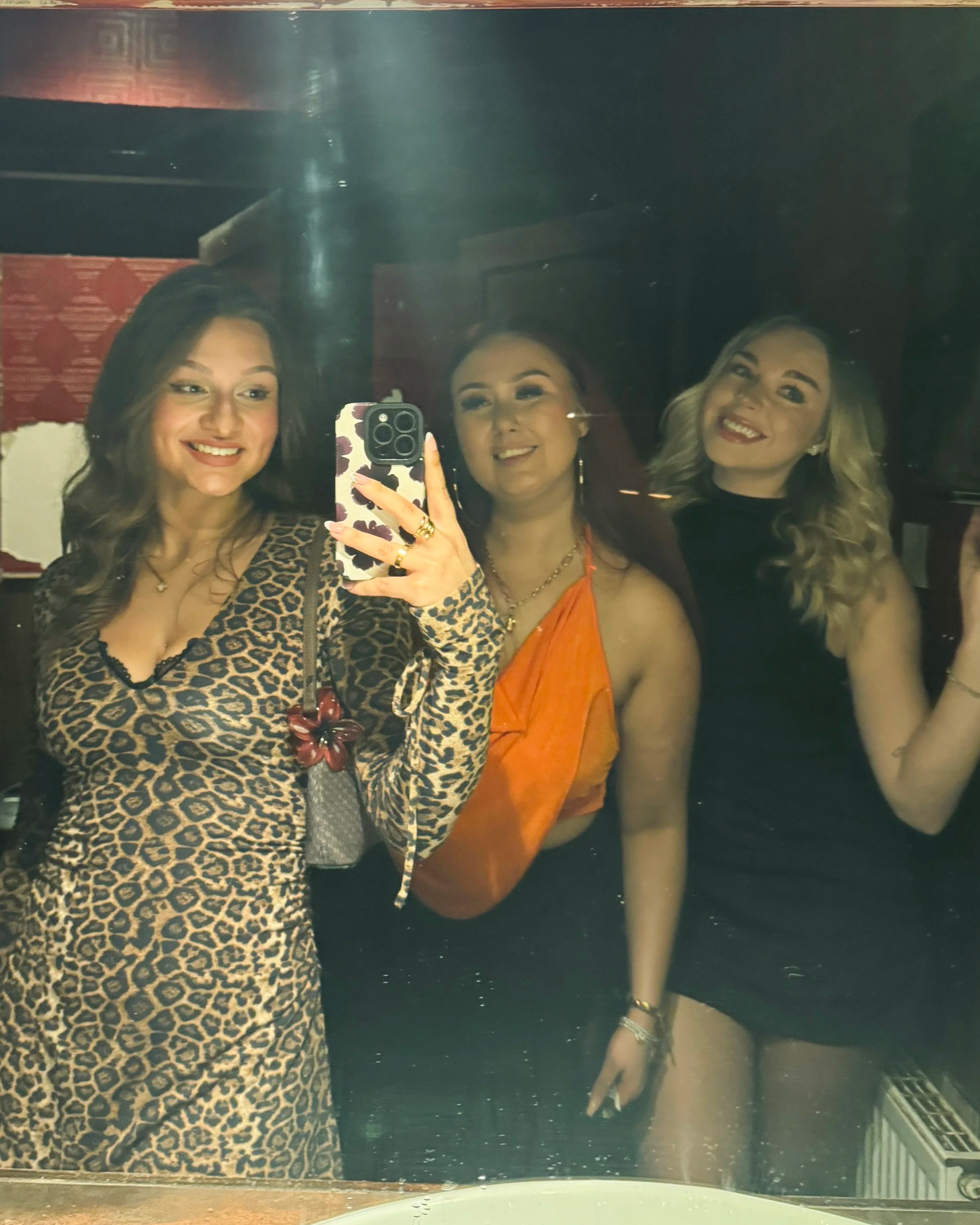Three girls posing and smiling in a mirror in a pub