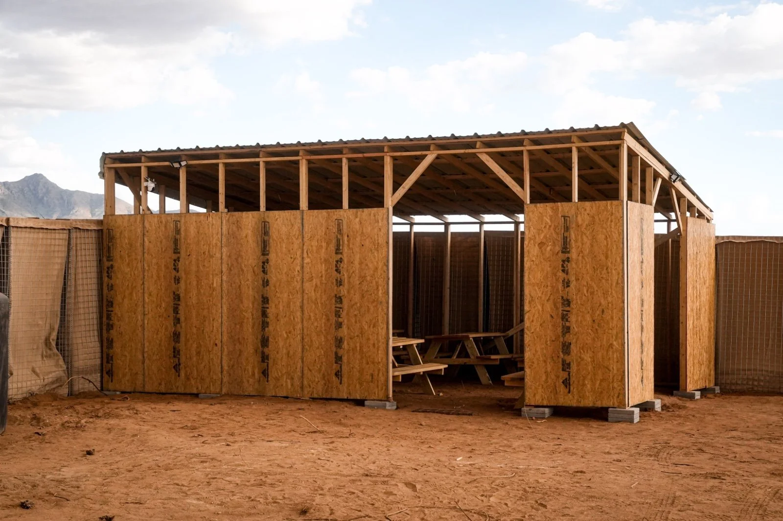 Bau einer Holzkonstruktion mit Holzwänden und Sitzgelegenheiten im Inneren, im Freien mit Bergen im Hintergrund.