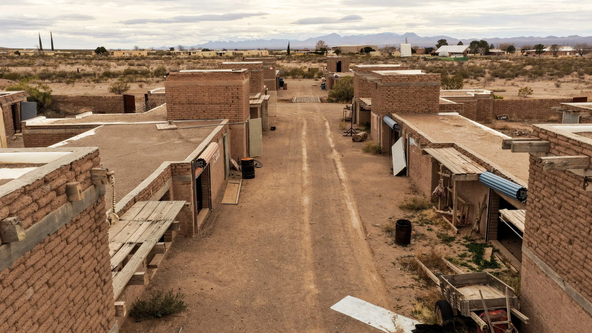 Panoramic view of an adobe-brick village with dirt lanes, flat-roofed buildings, desert scrub, and mountains in the distance