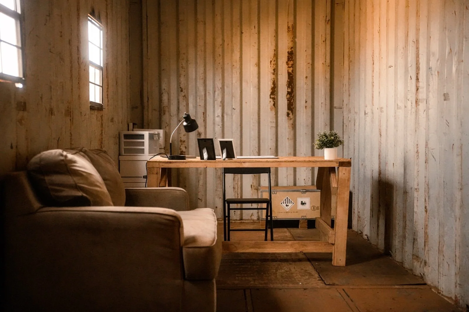 Ein schlichtes Arbeitszimmer mit Holzwand und Holztisch, einem schwarzen Stuhl, Sofas und einem kleinen Fenster mit natürlichem Licht.