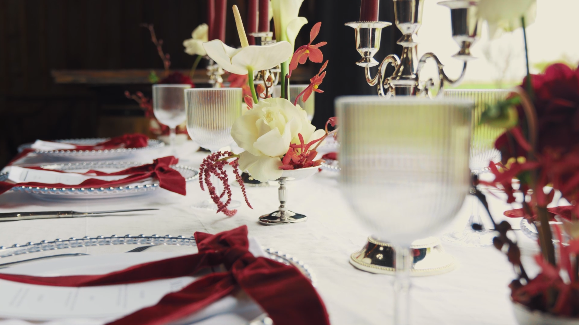 A decorated dining table with floral centerpieces, glassware, plates with red ribbons, and candlesticks, set for a formal meal.